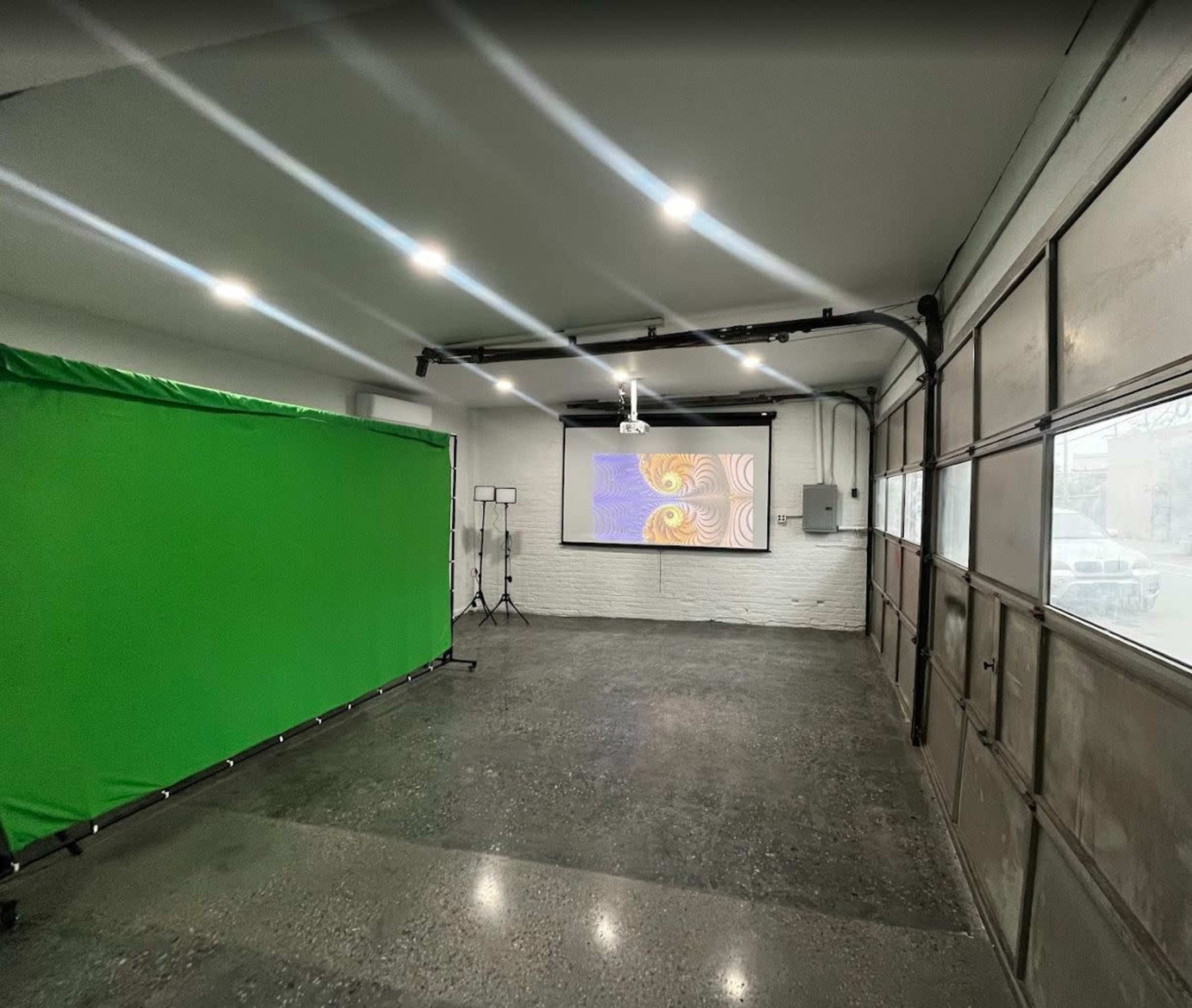 The image shows an empty room with a green screen setup on one side and a projector displaying colorful graphics on the wall opposite.