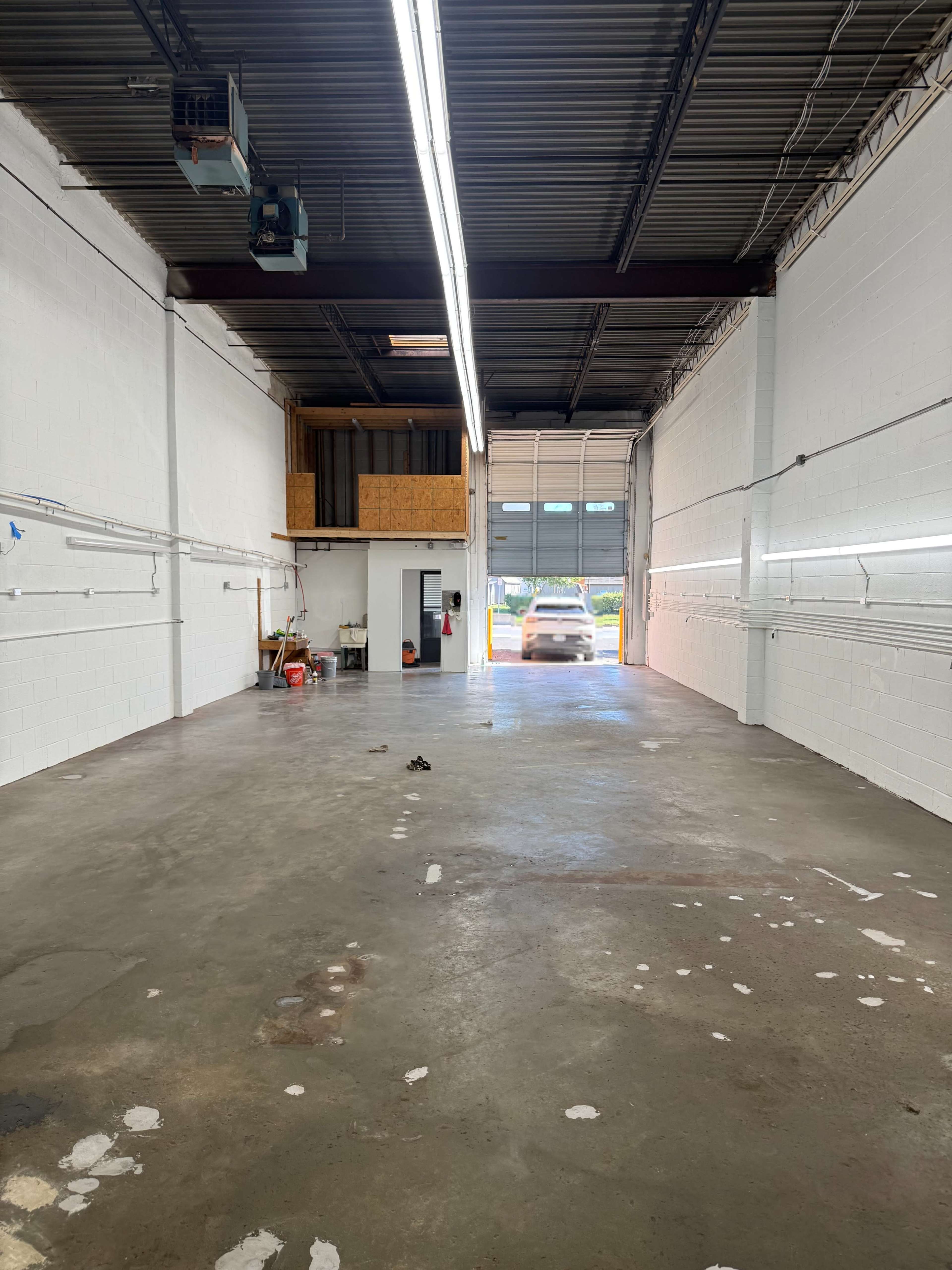 The image shows an empty warehouse interior with white walls, a concrete floor, and a large open loading door at the far end.