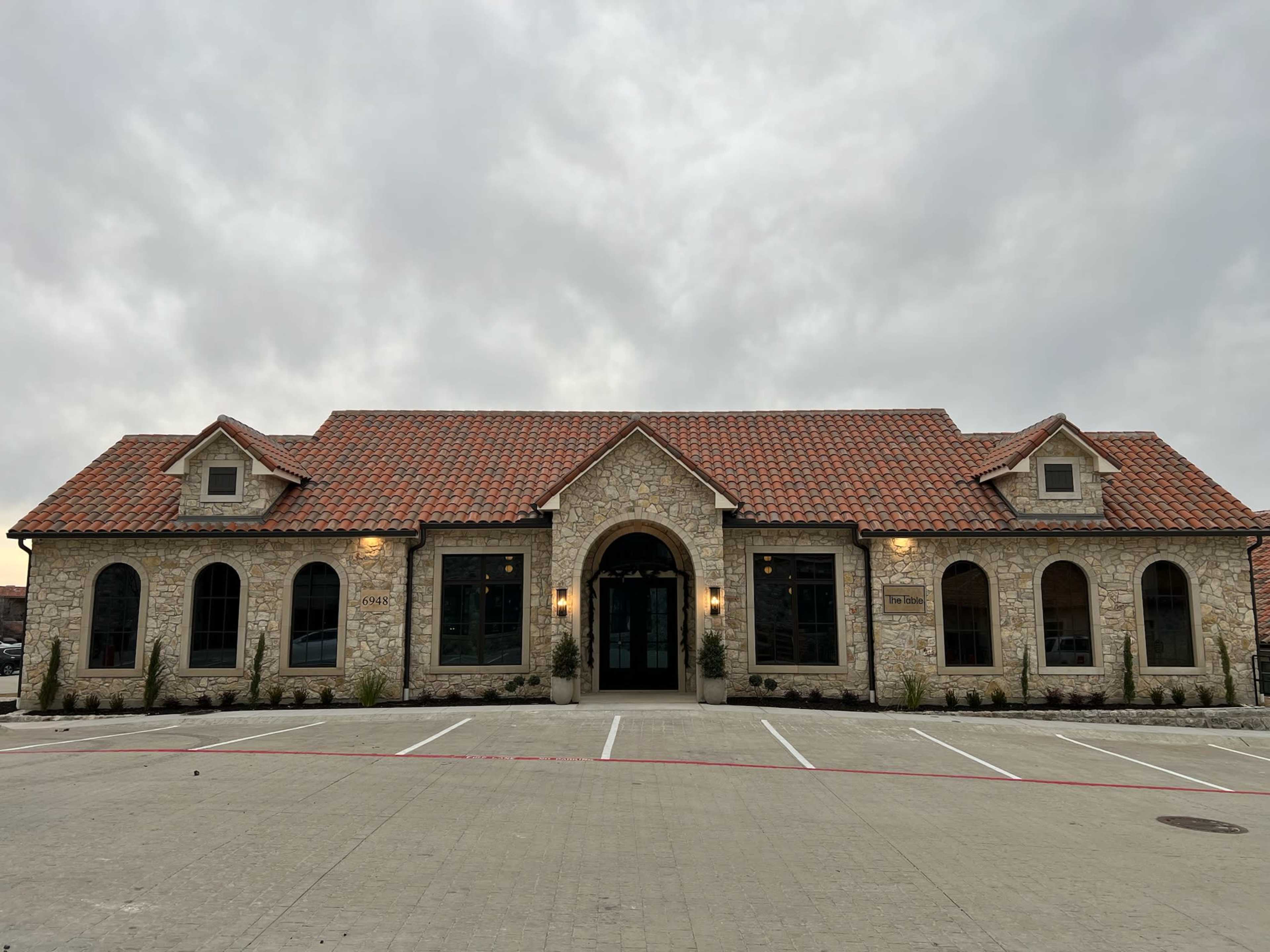 The building features a stone exterior with a tiled roof and arched windows, standing in an empty parking lot.