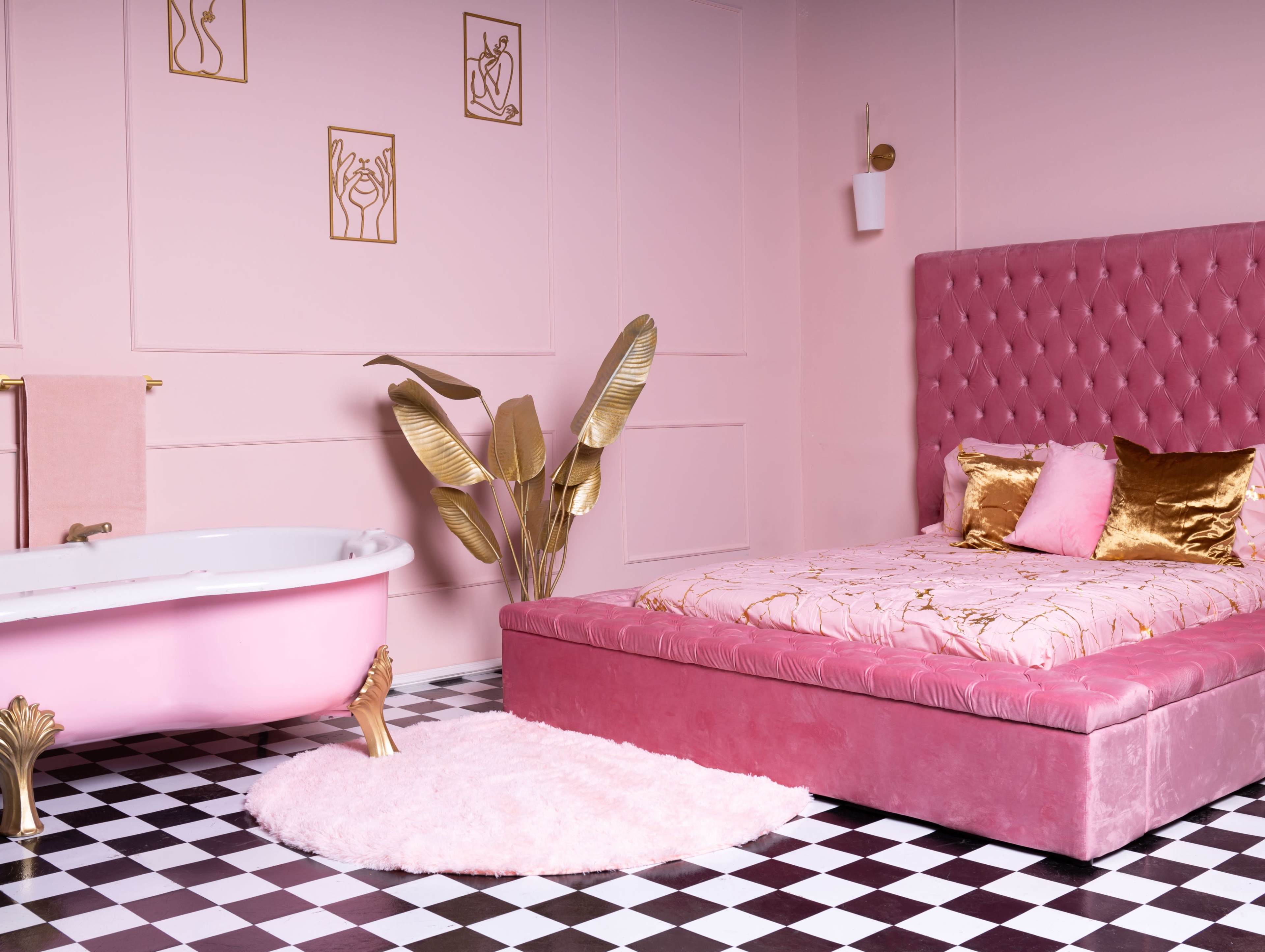 A pink bedroom with a velvet bed, a clawfoot bathtub, and decorative gold accents, set against a black and white checkered floor.