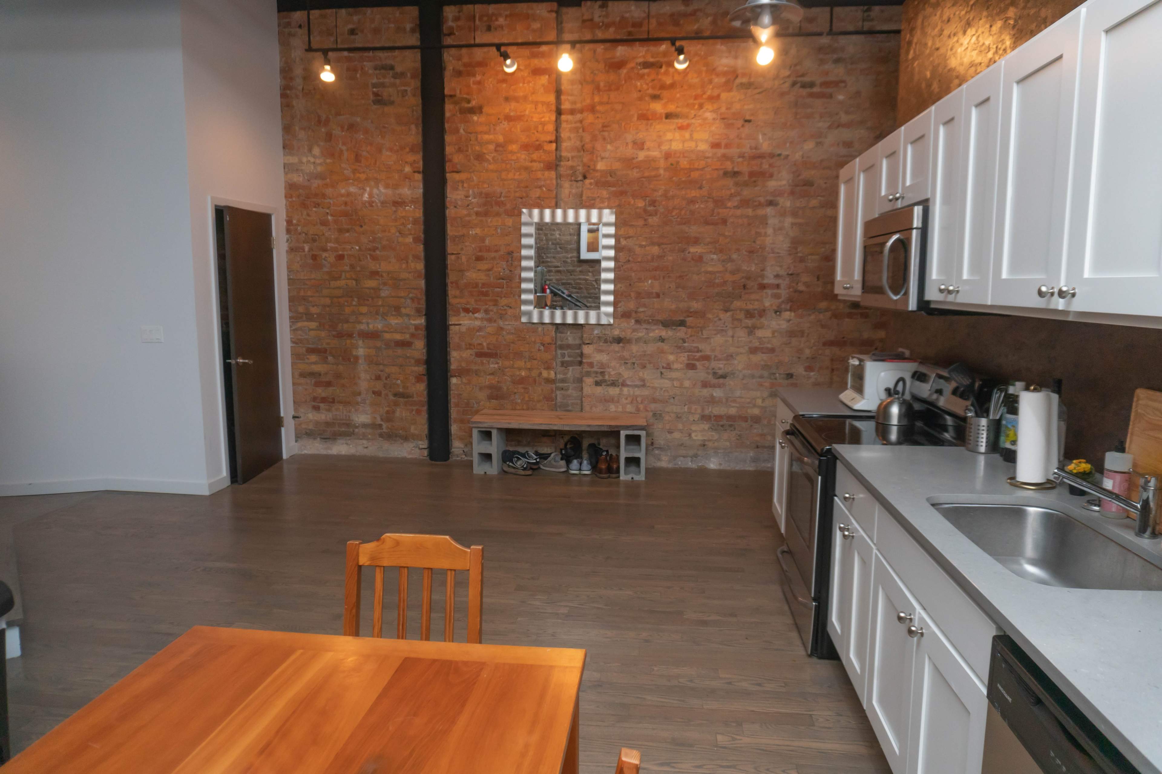 A modern kitchen and dining area featuring exposed brick walls, a wooden dining table, and stainless steel appliances.