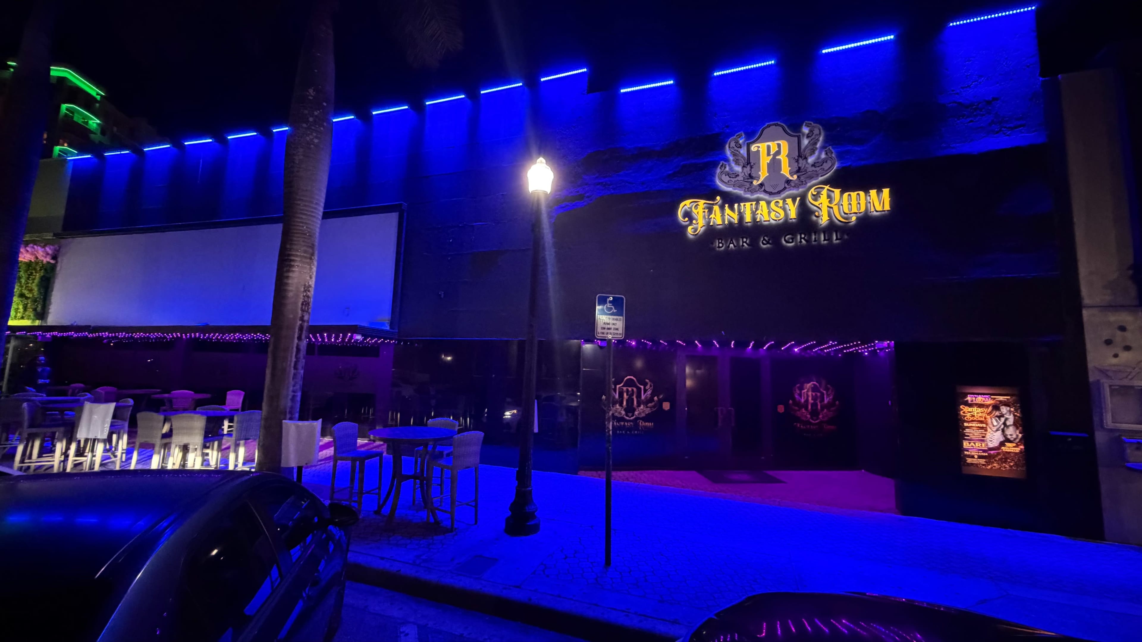 The image shows the exterior of the Fantasy Room Bar & Grill, illuminated by blue and purple lights at night.