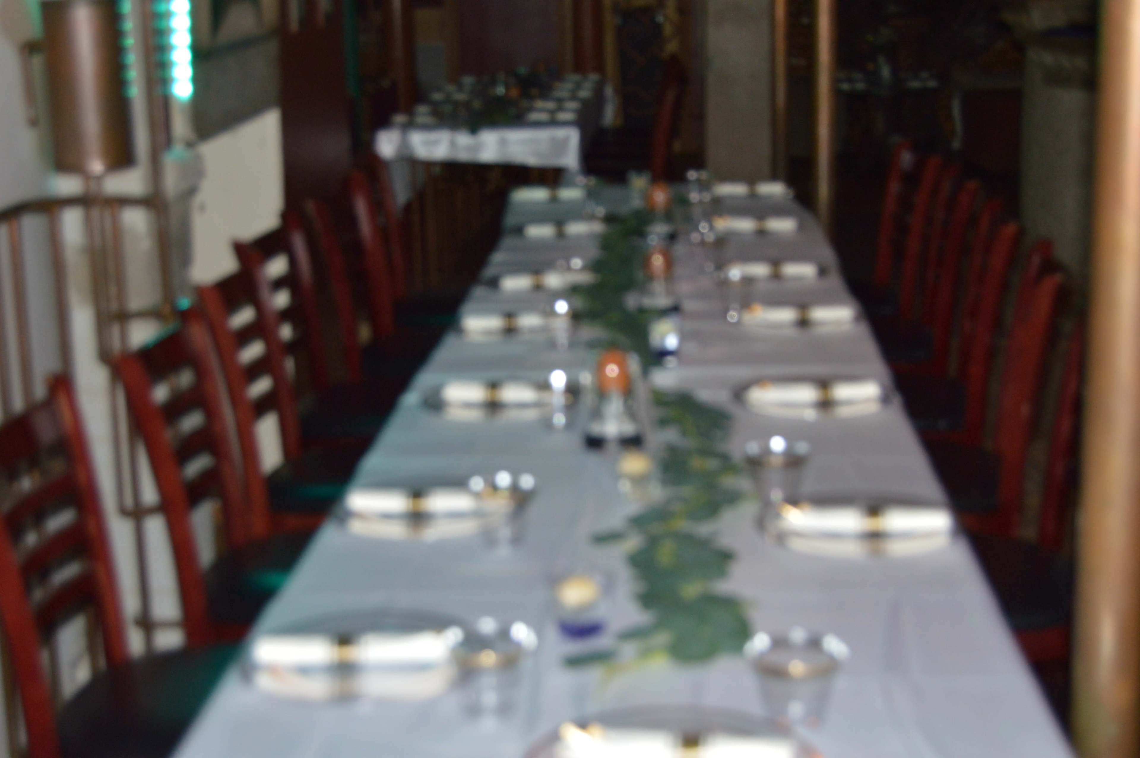 A long dining table is set with plates, cutlery, and a green centerpiece in a restaurant.