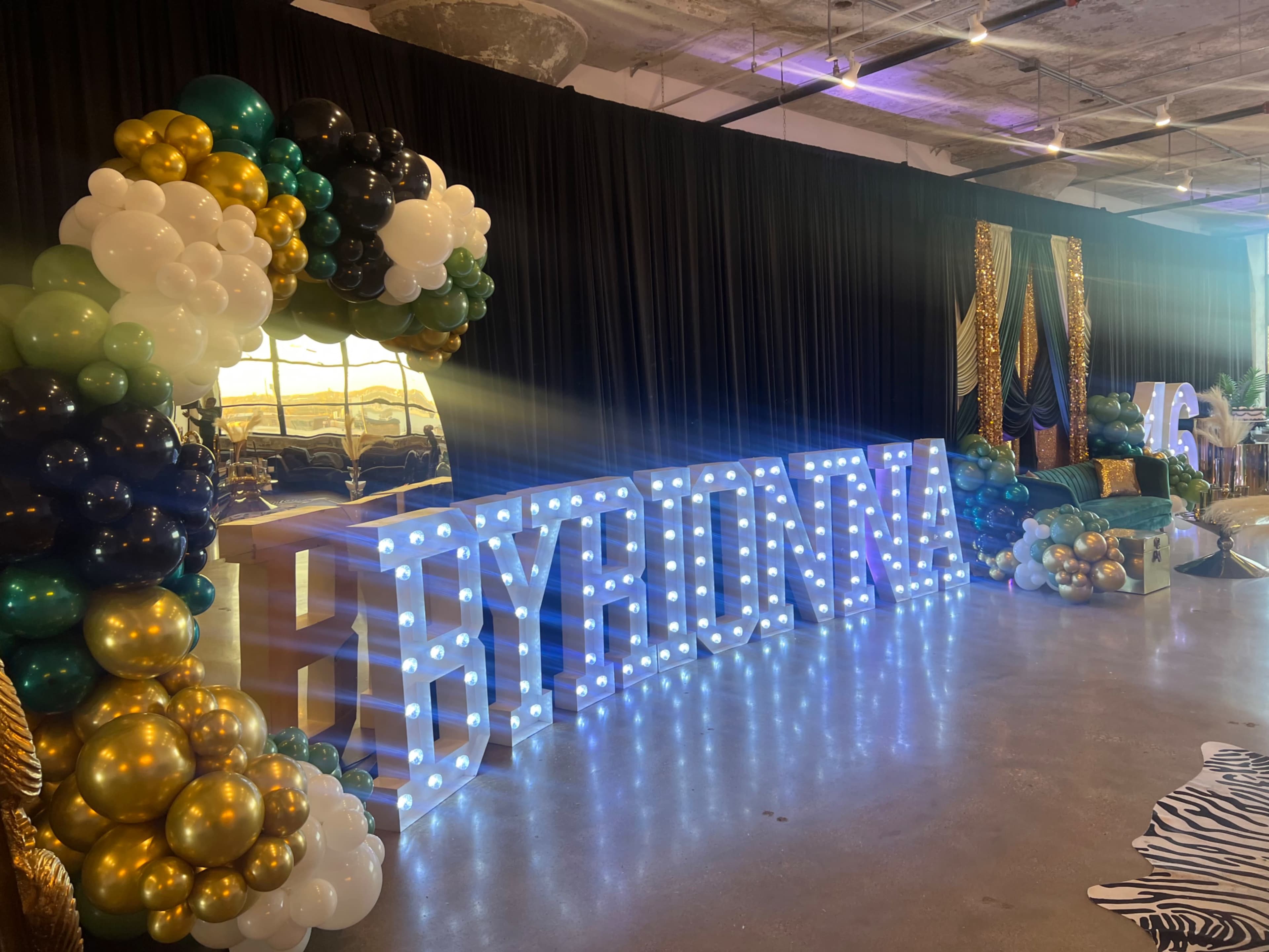 The image shows a decorated event space featuring a large balloon arch and illuminated lettering that spells "HYBRID 2023."