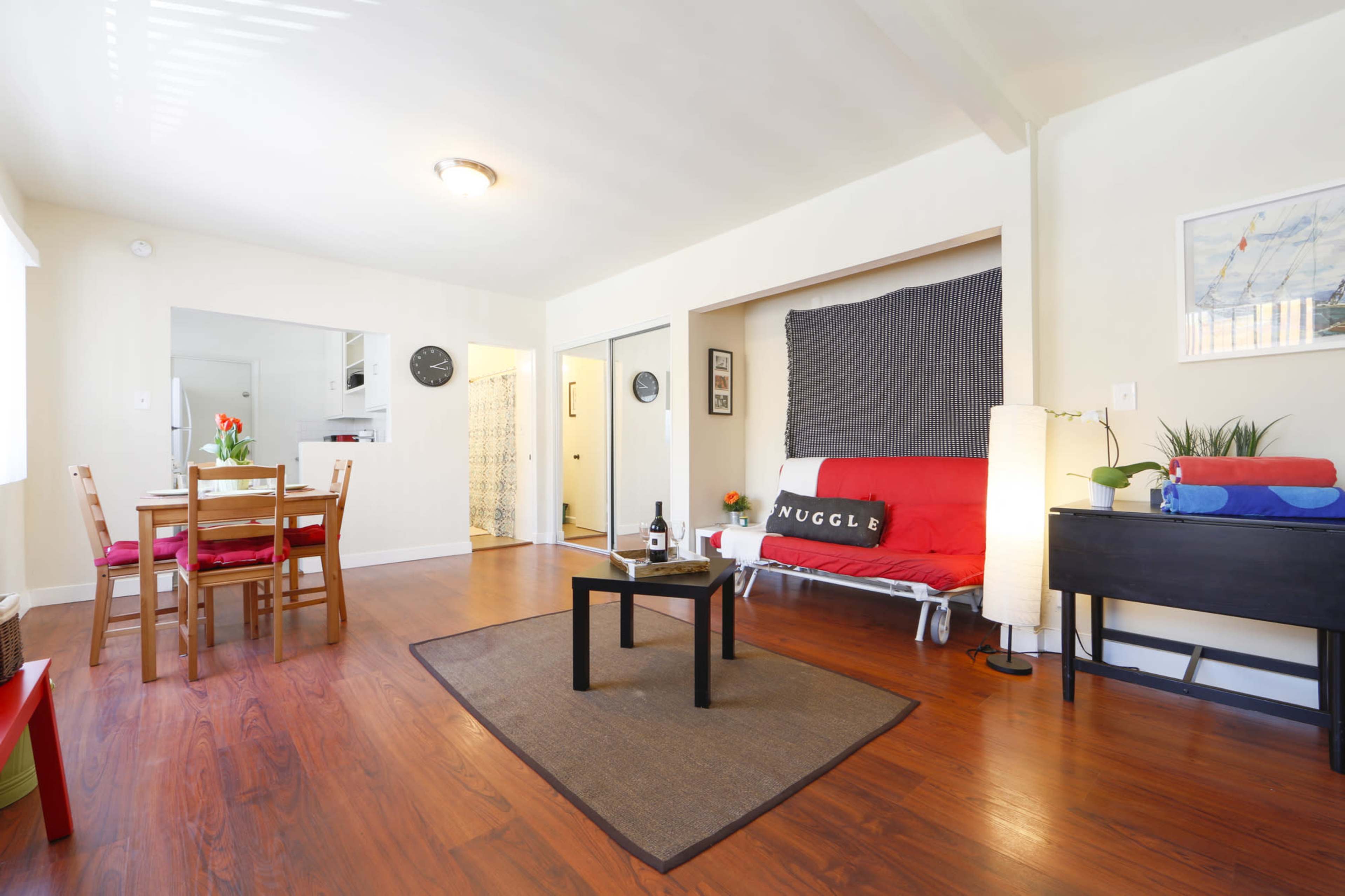 A well-lit living space with a dining area, a futon sofa, and a small table situated on a hardwood floor.