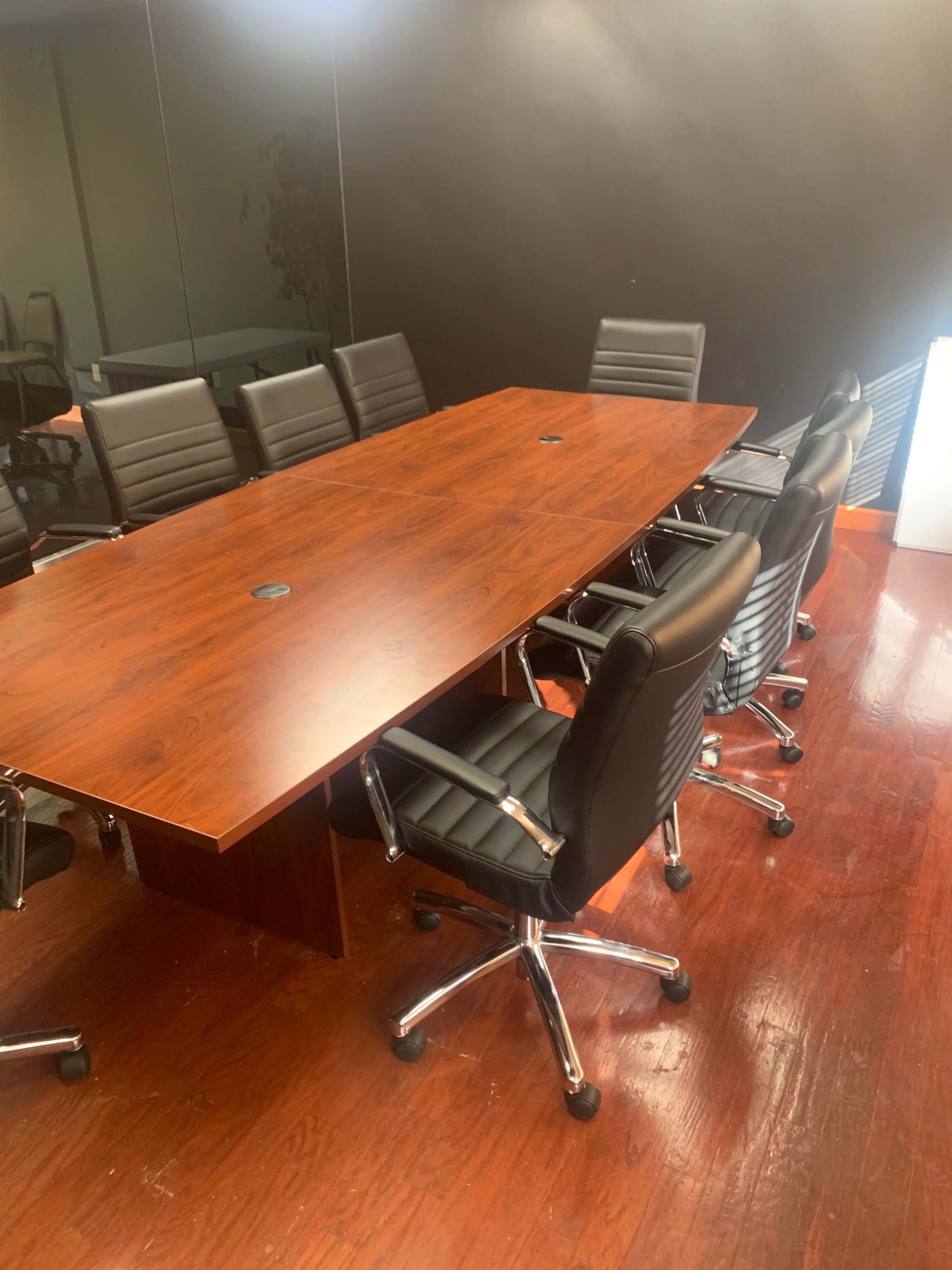 A large wooden conference table is surrounded by black leather swivel chairs in a corporate meeting room.