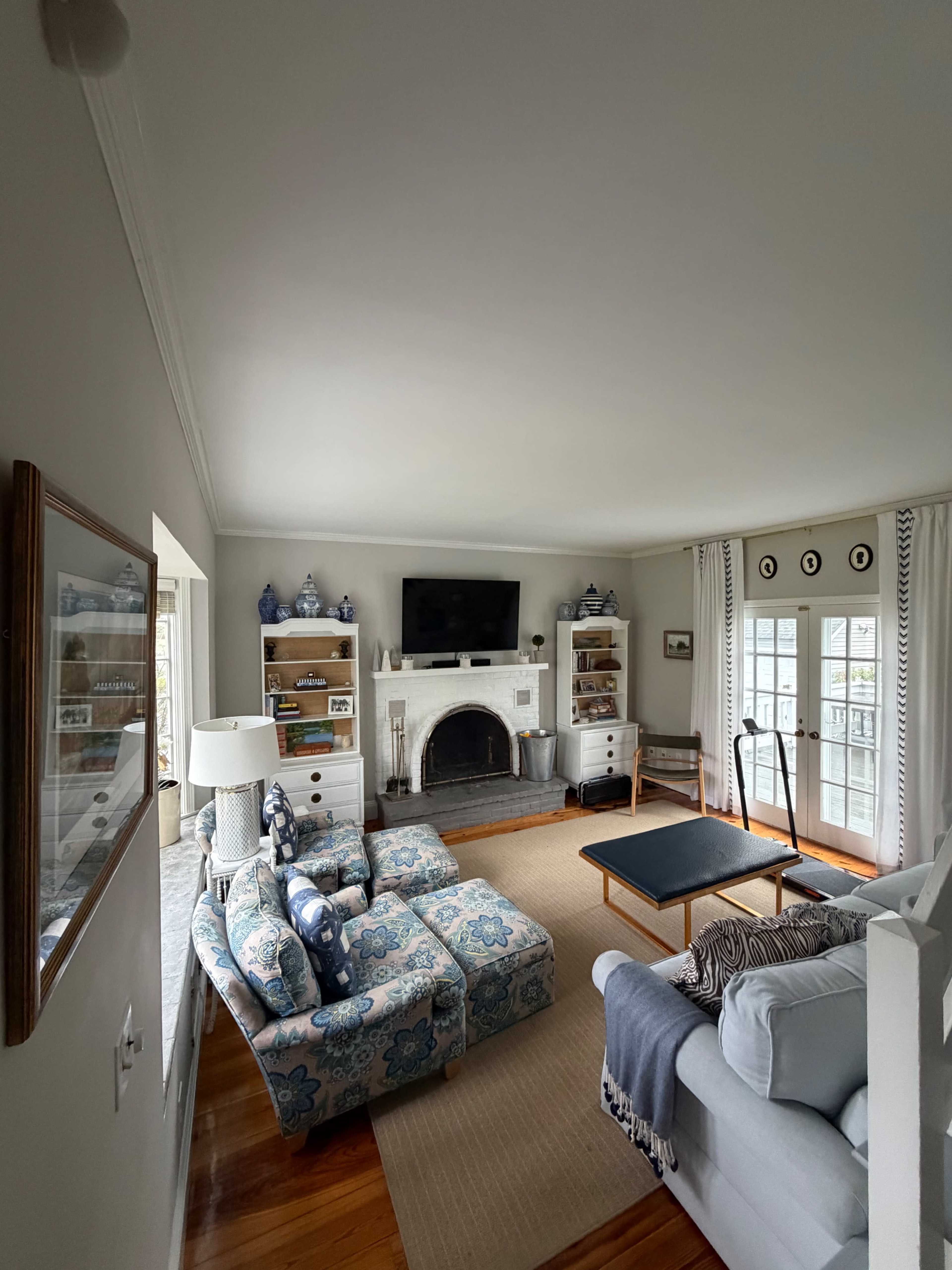 The image shows a living room featuring a blue floral-patterned armchair and sofa, a coffee table, a fireplace, and built-in shelving with decorative items.