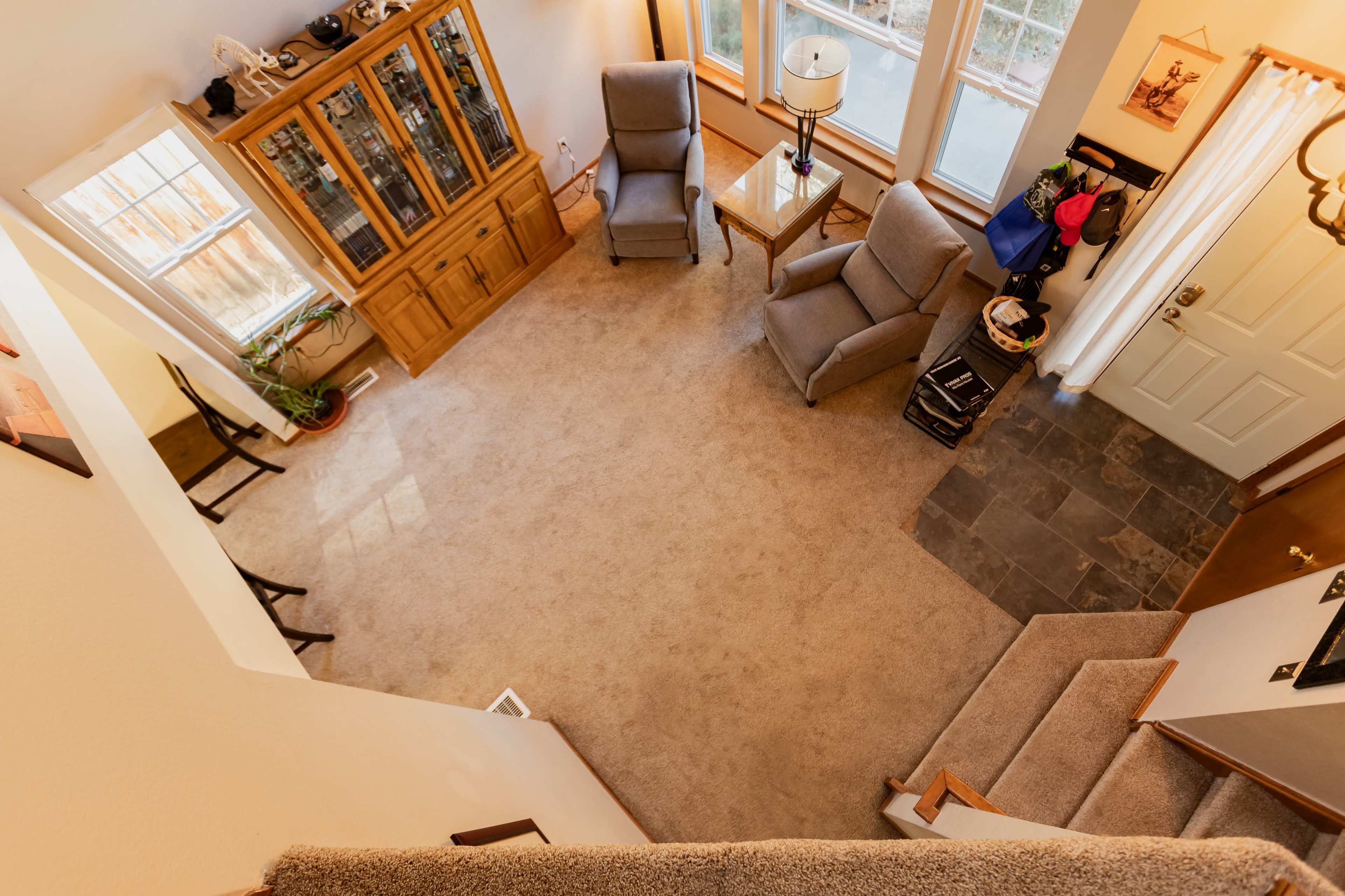 The image shows an overhead view of a cozy living room area featuring two armchairs, a small table, a cabinet, and a staircase leading to the upper floor.