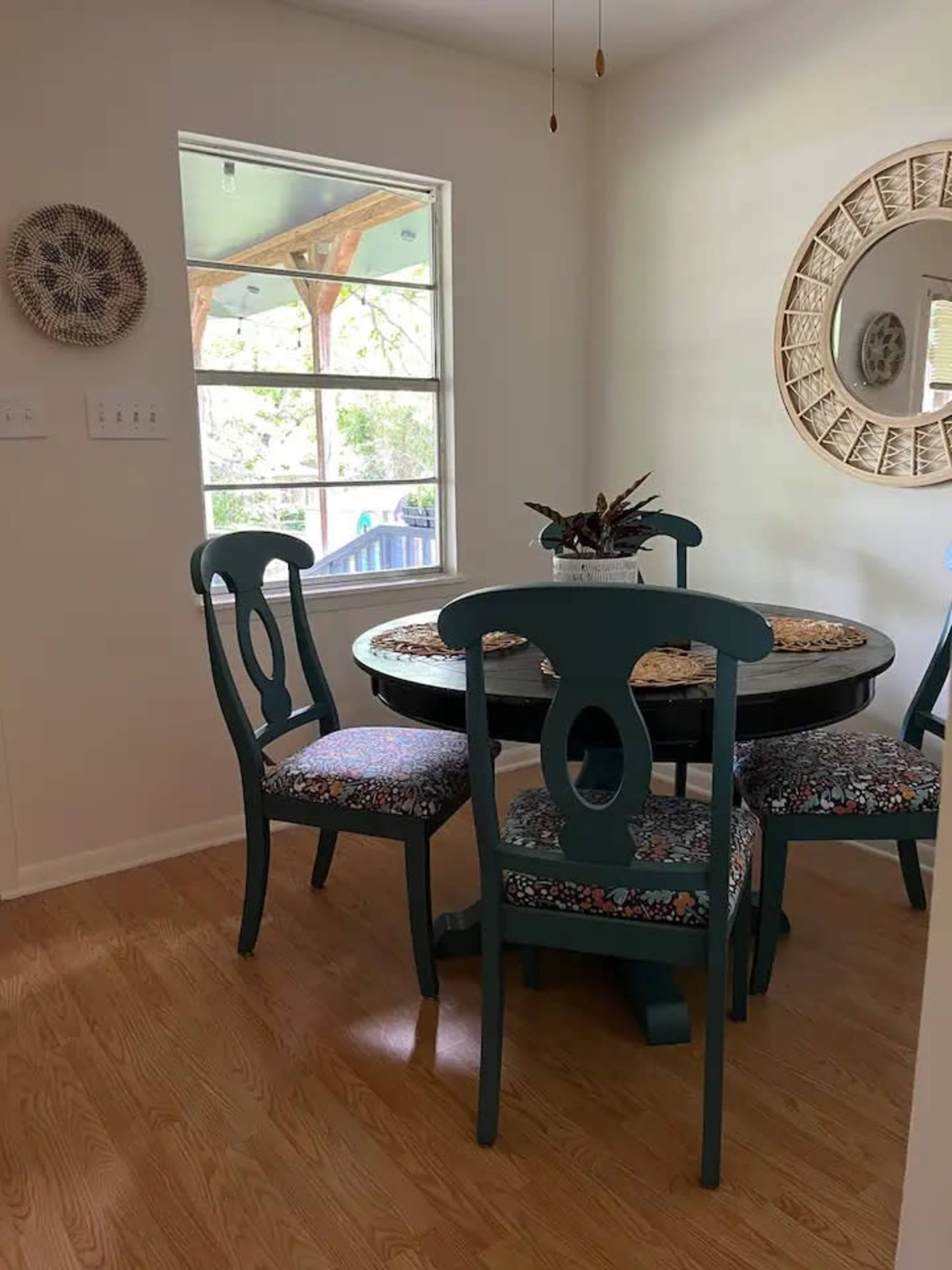 A small dining area features a round table with four teal chairs and floral-patterned upholstery, positioned near a window.