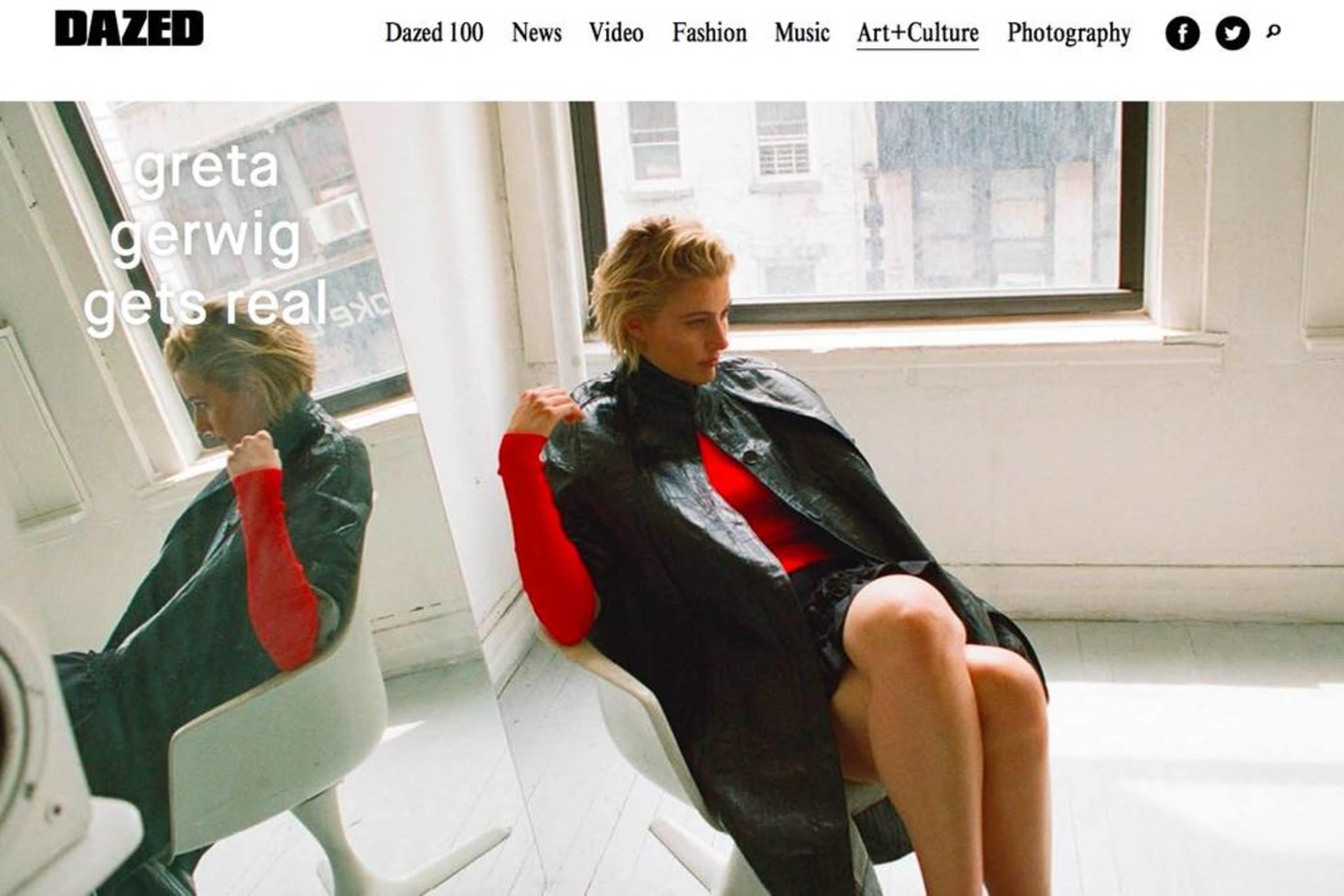 A woman sitting in a chair by a window, wearing a black coat over a red top, poses for the camera in a well-lit room.
