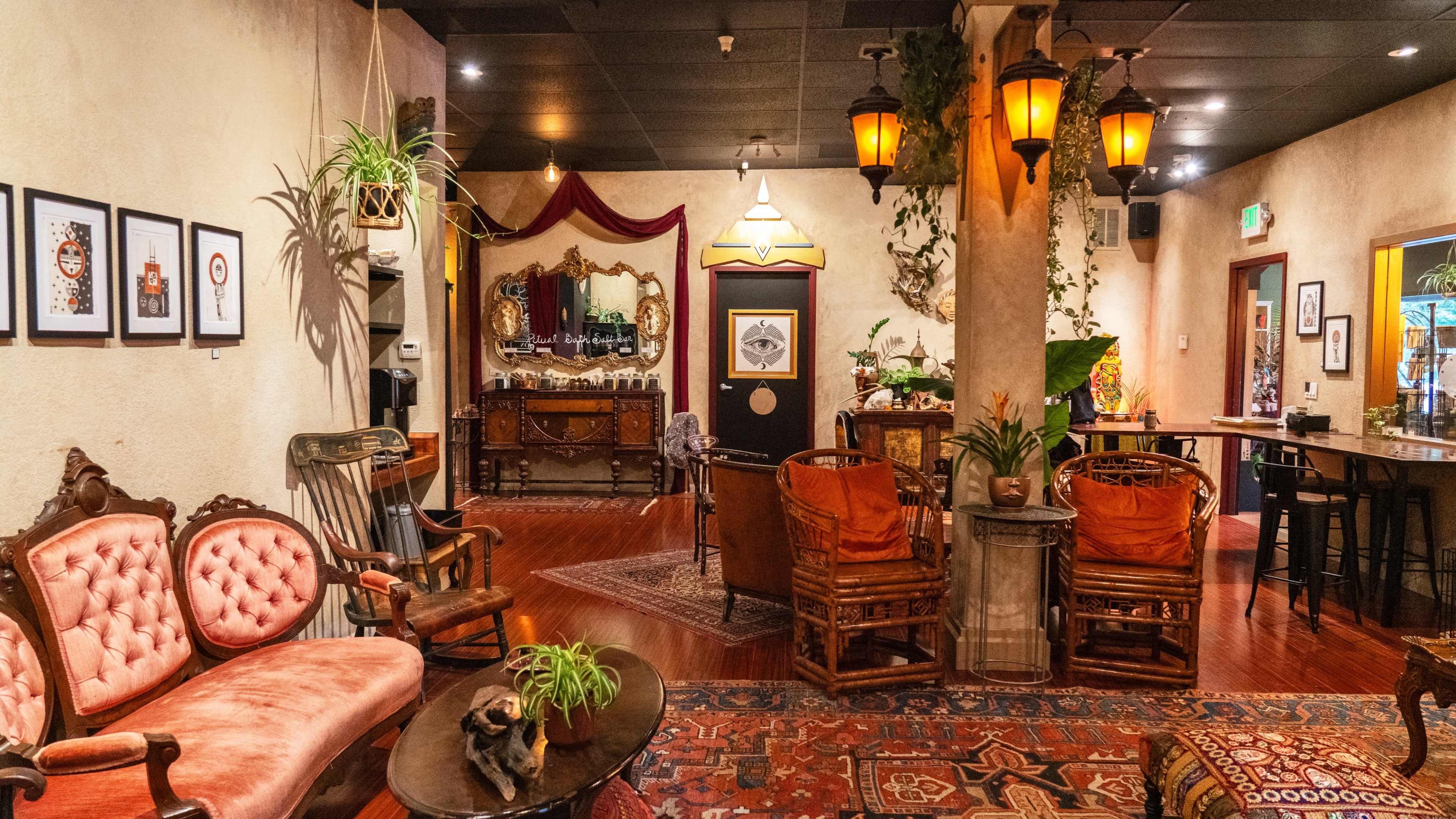The image shows a cozy interior of a vintage-style lounge with ornate furniture, decorative plants, and warm lighting.