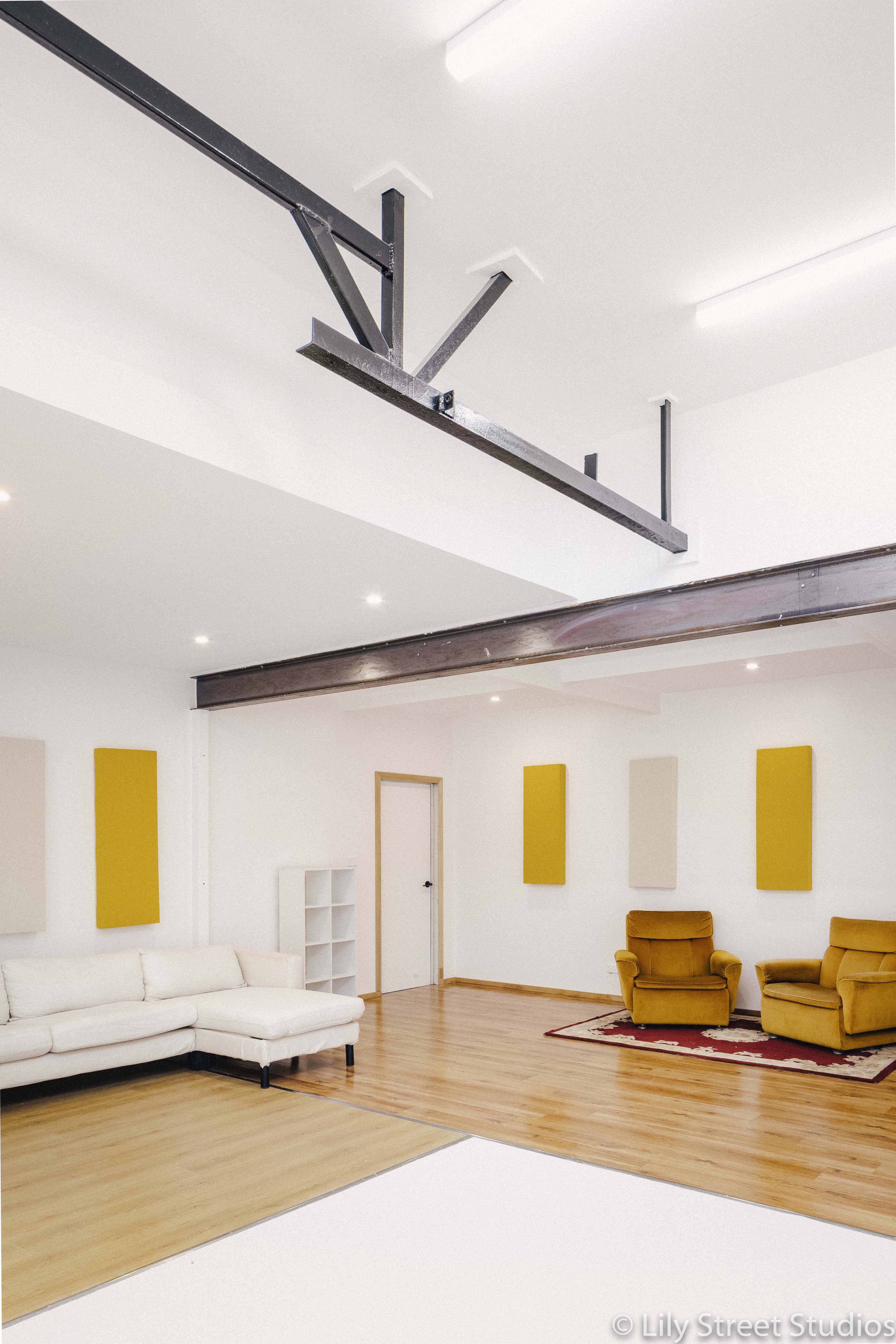 The image shows a spacious interior with a sofa, two armchairs, and a wooden floor illuminated by fluorescent lighting.