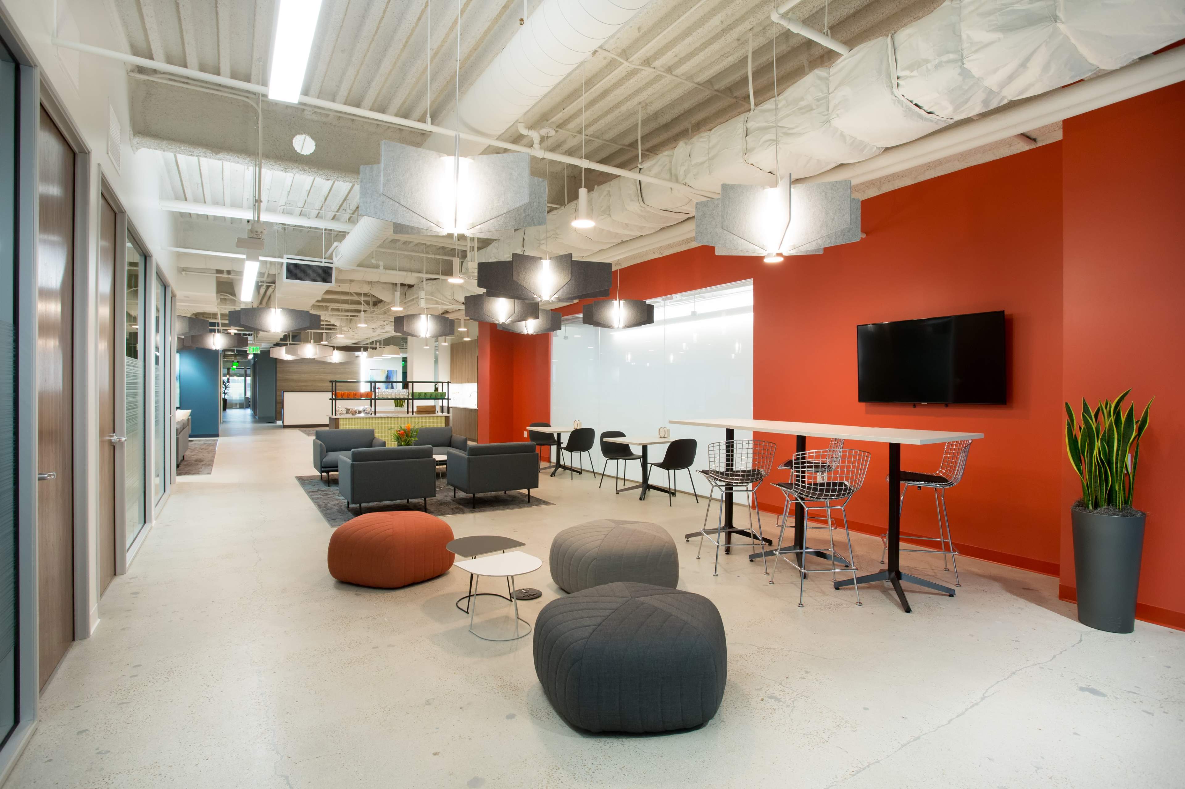 An office space features modern furniture, casual seating arrangements, and a combination of red and gray walls.