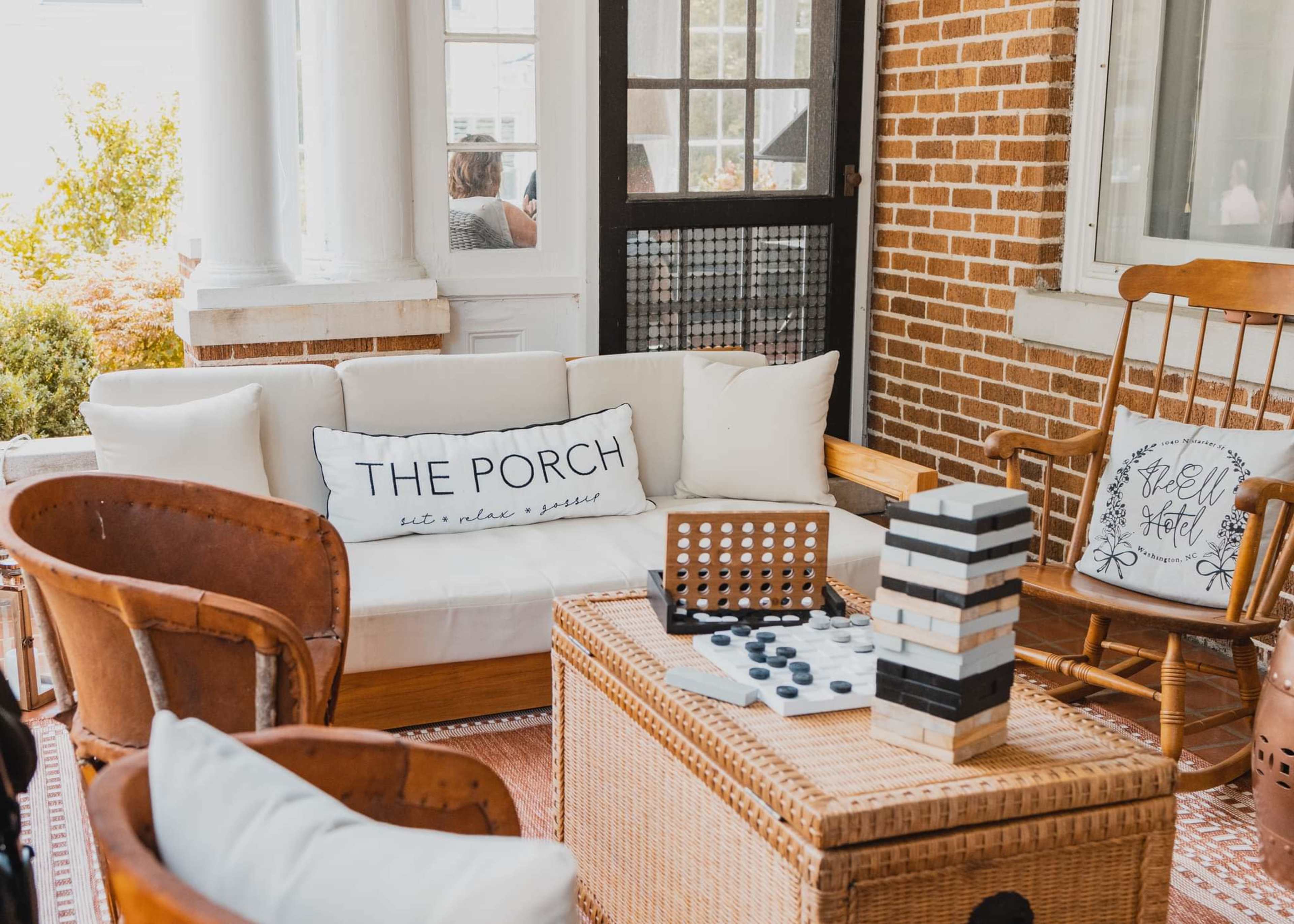 A cozy porch setting with a white sofa, wicker furniture, and games like checkers and Jenga on a coffee table.