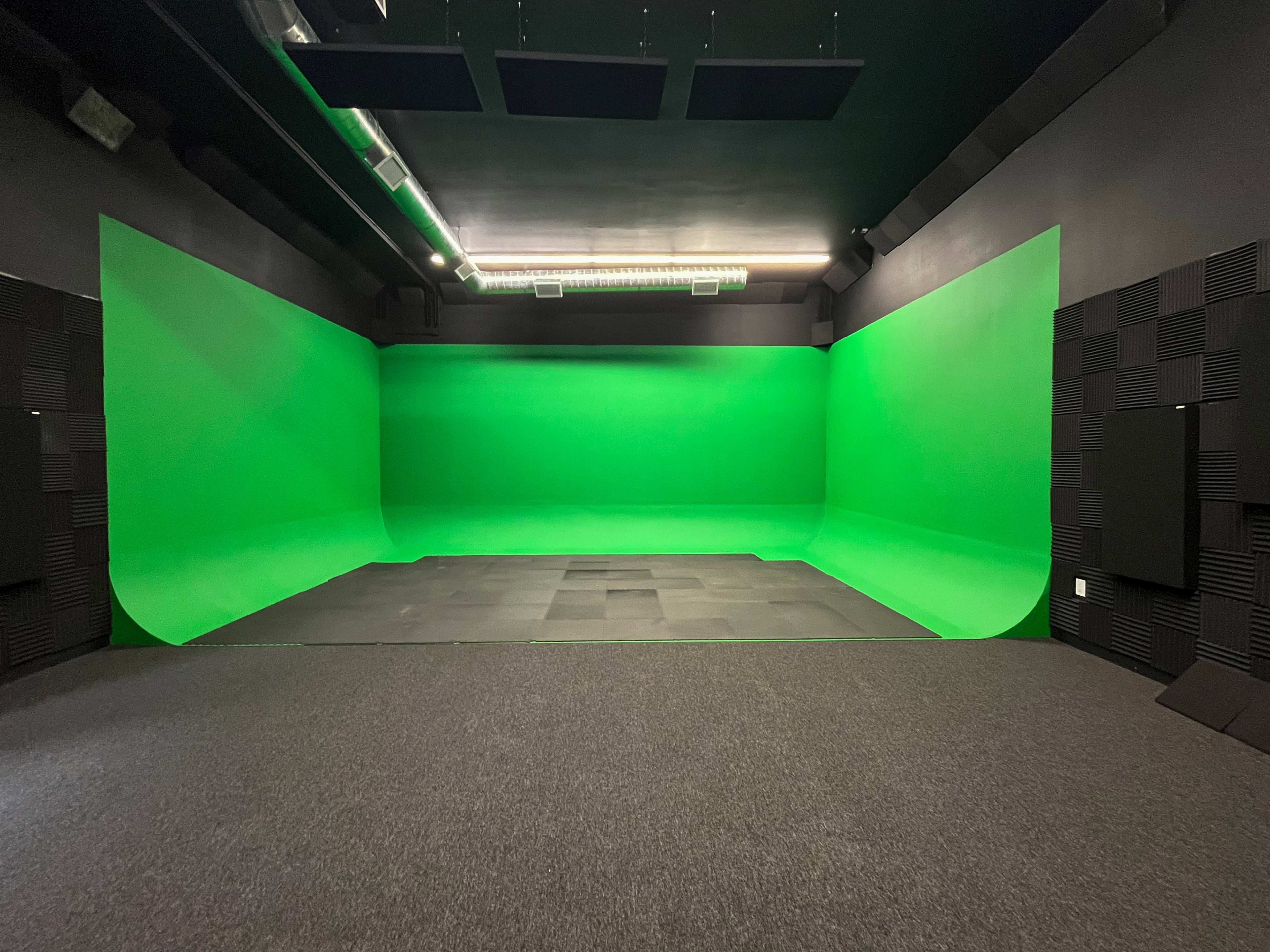 A studio space featuring green screen walls and a seamless green floor.