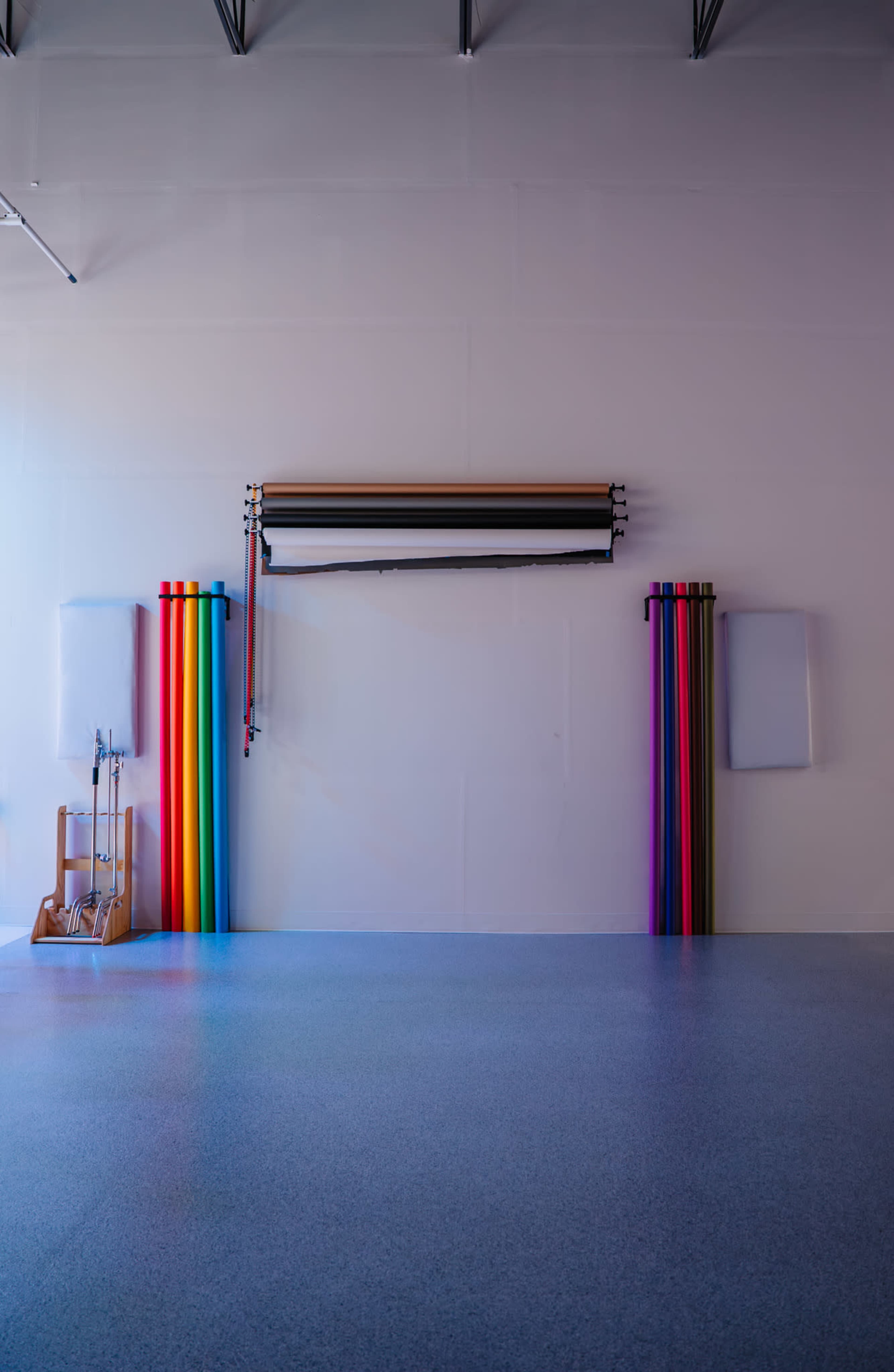 The image shows a large, empty studio space with a backdrop roll located in the center, flanked by vertical rolls of colored paper on both sides.