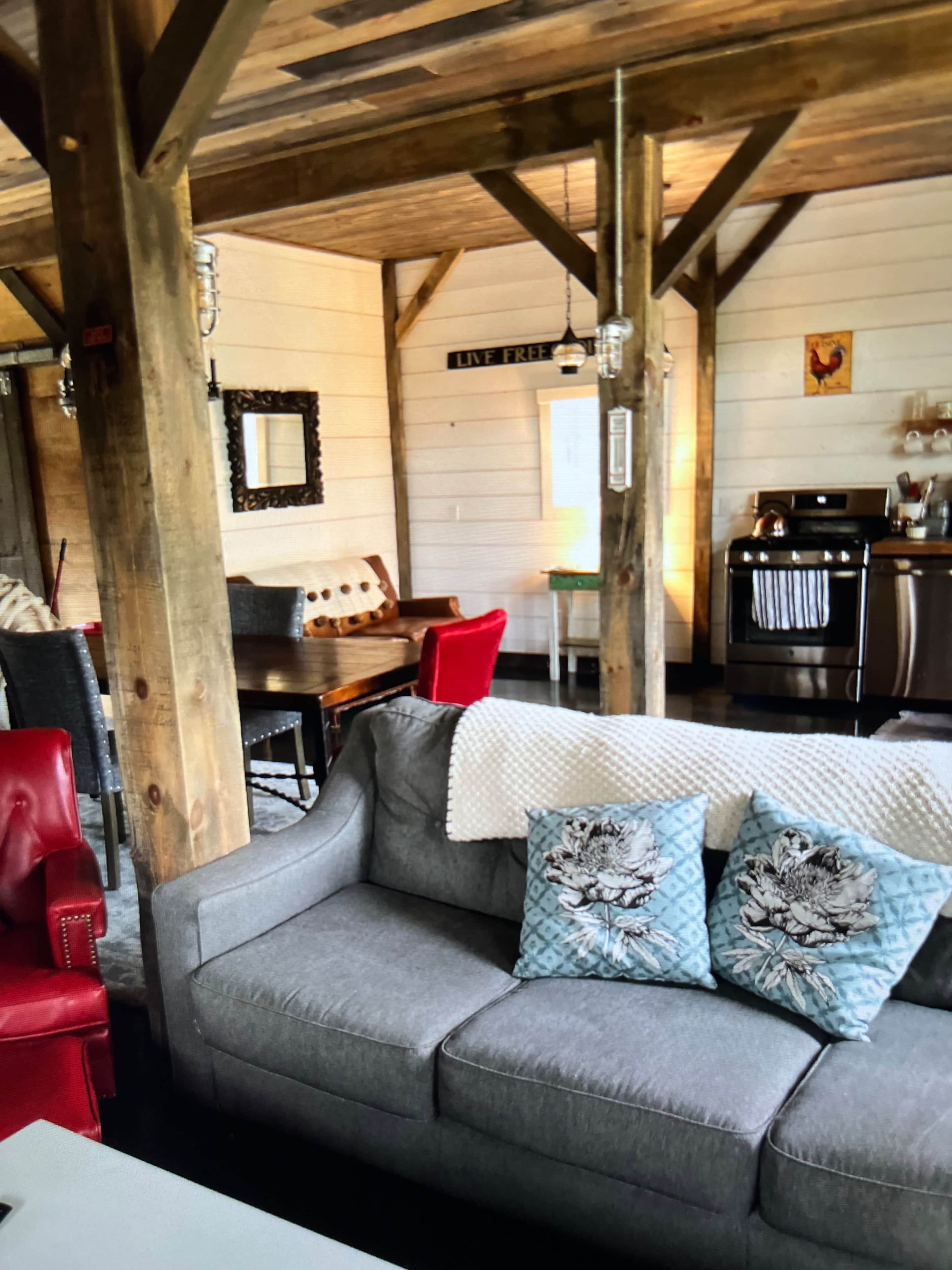 A cozy living space with a gray sofa adorned with decorative pillows, a wooden dining table, and a kitchen area featuring stainless steel appliances.