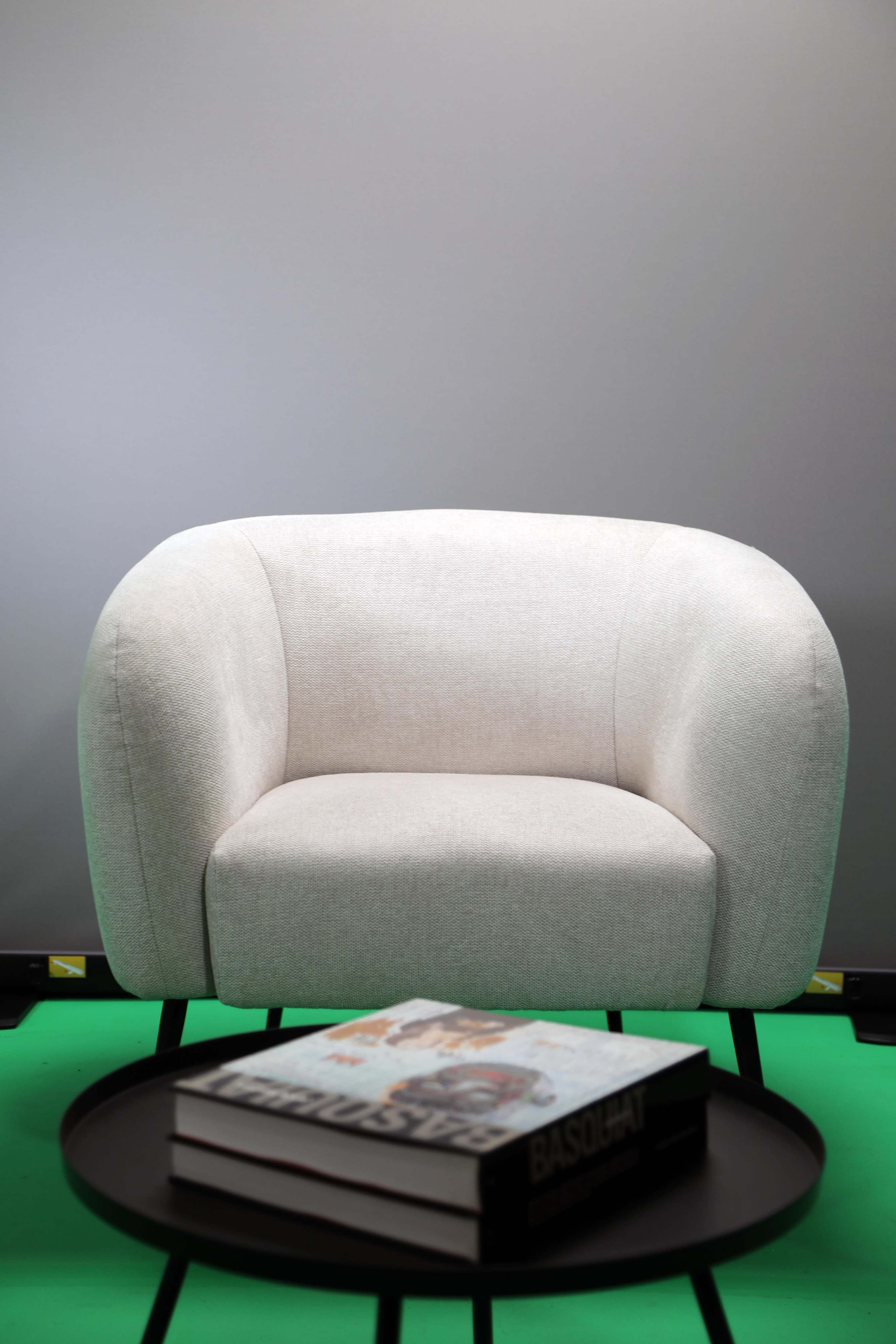 A cream-colored upholstered chair sits on a green surface beside a stack of books on a black table.