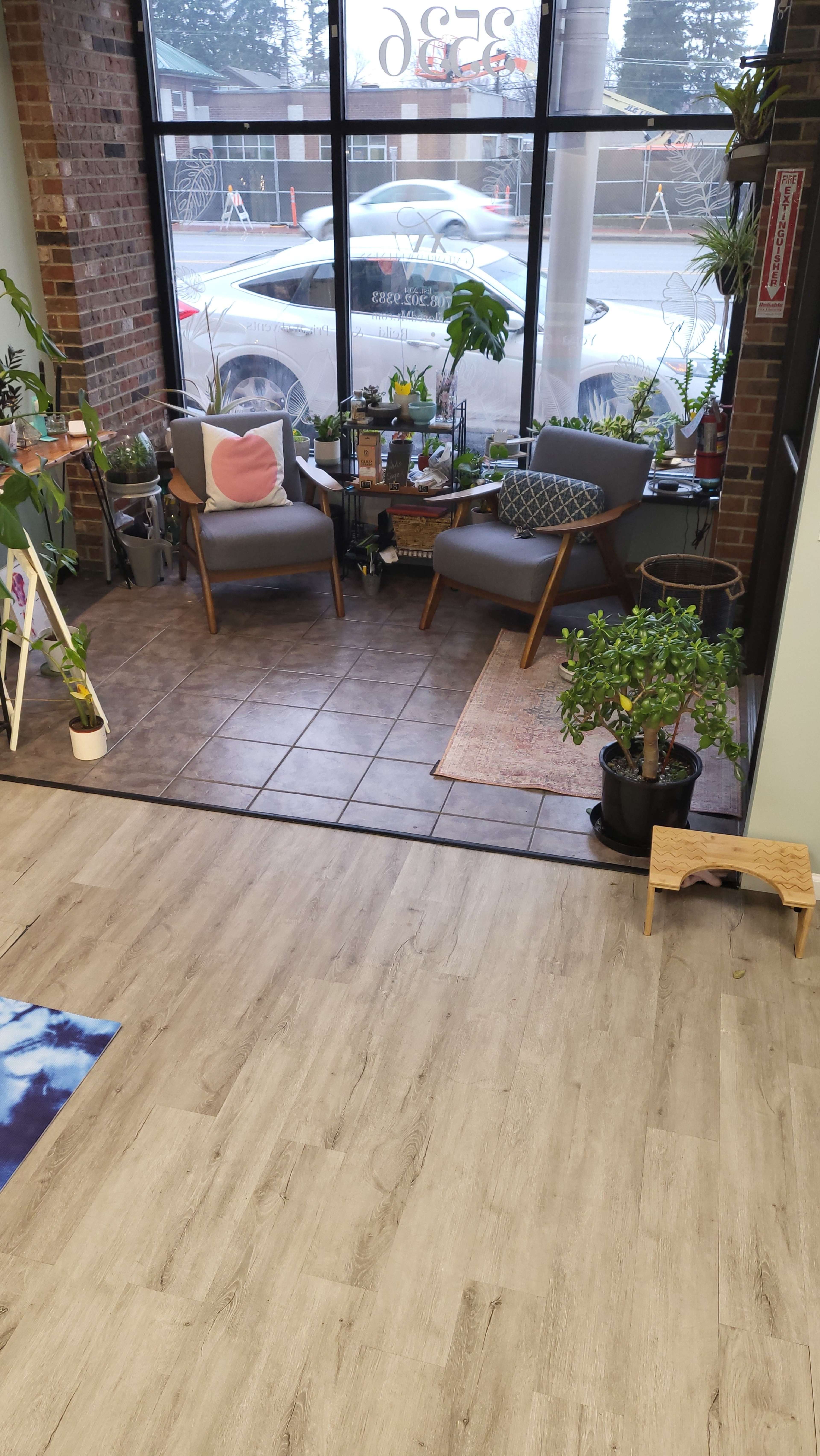 A cozy seating area with two armchairs and various potted plants in front of a large window.