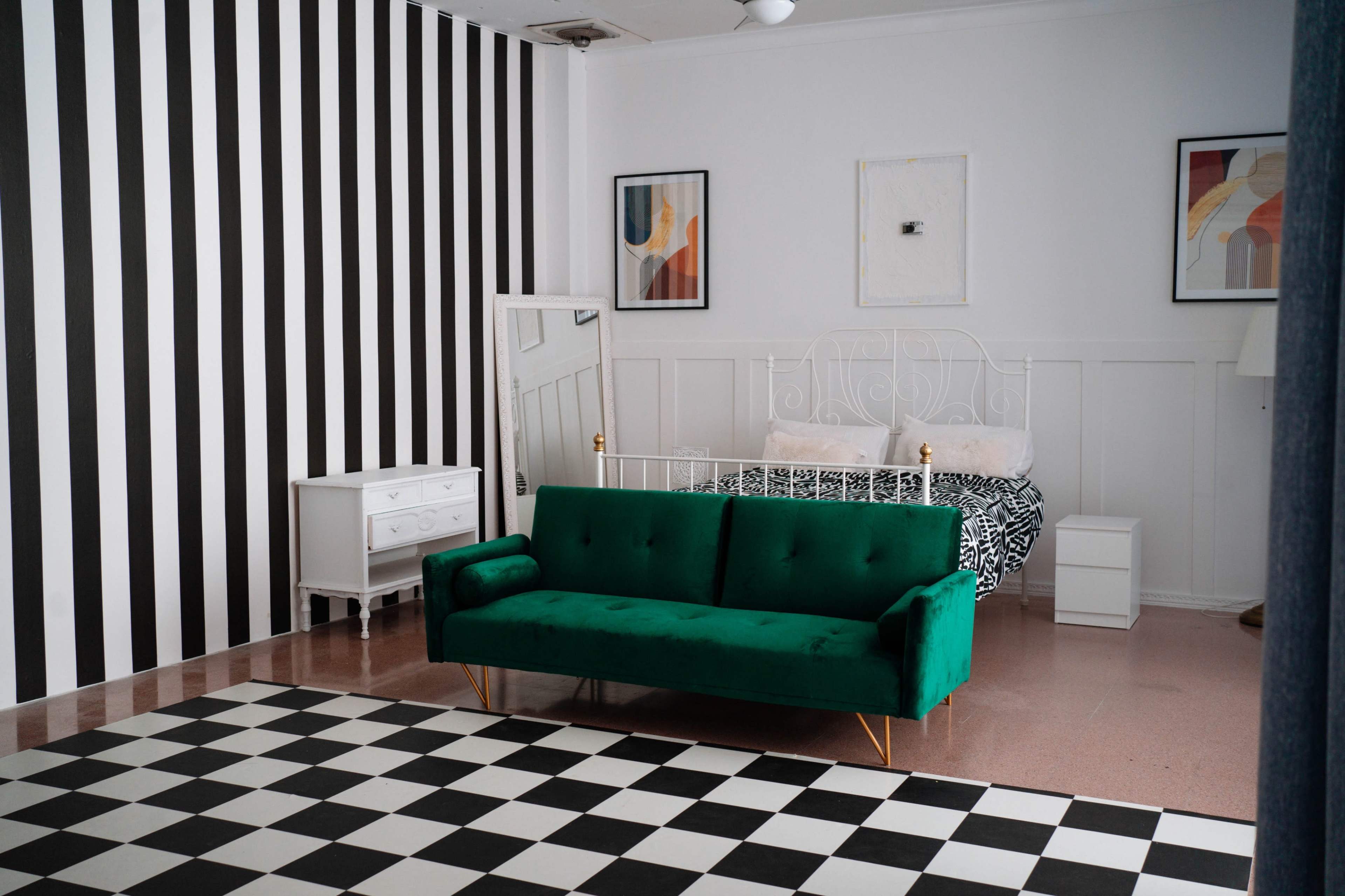 A room features black and white striped walls, a green couch, a checkered floor, and a bed with patterned bedding.