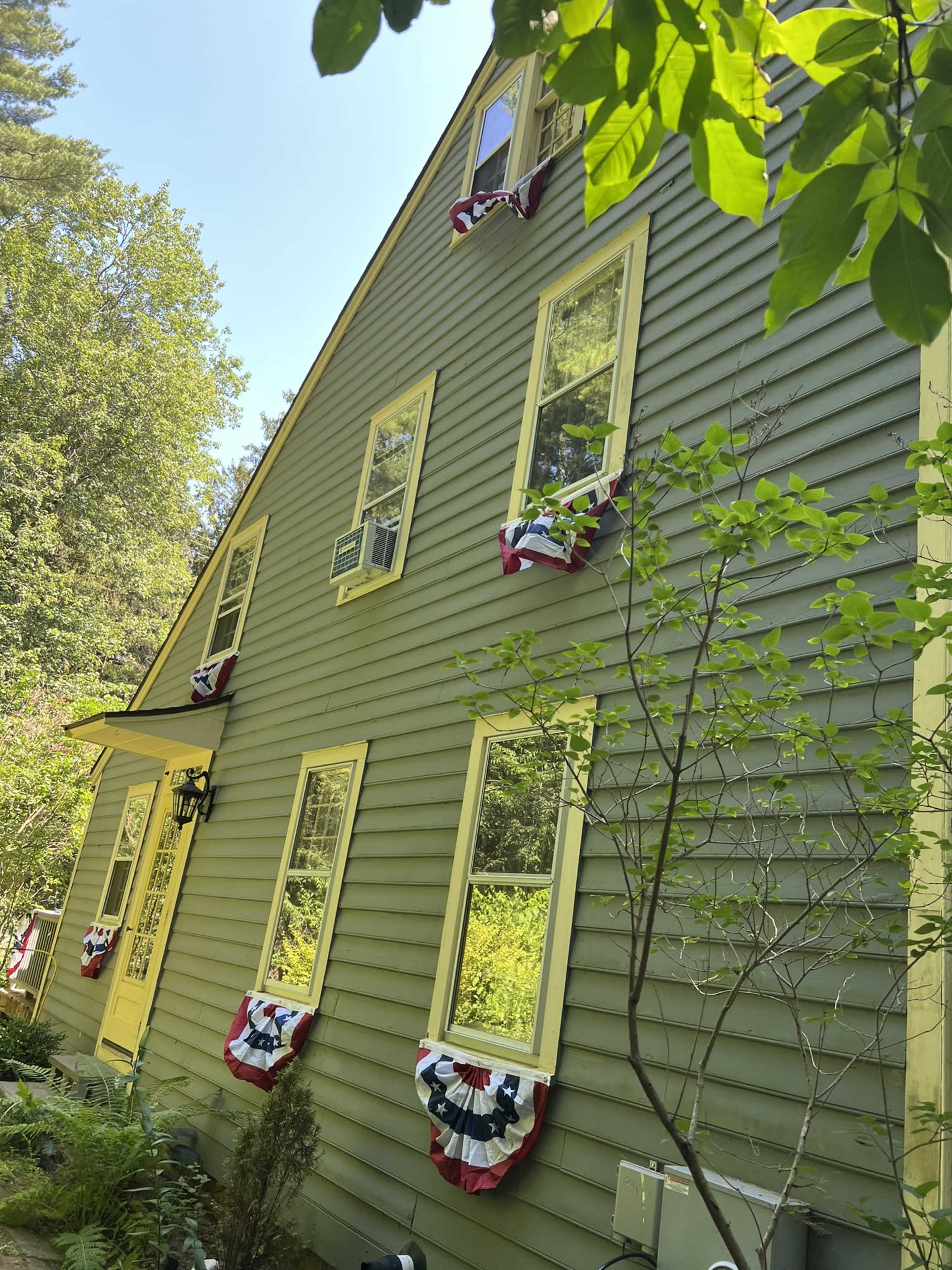 The image shows a green house with yellow trim, featuring several windows adorned with red, white, and blue bunting.