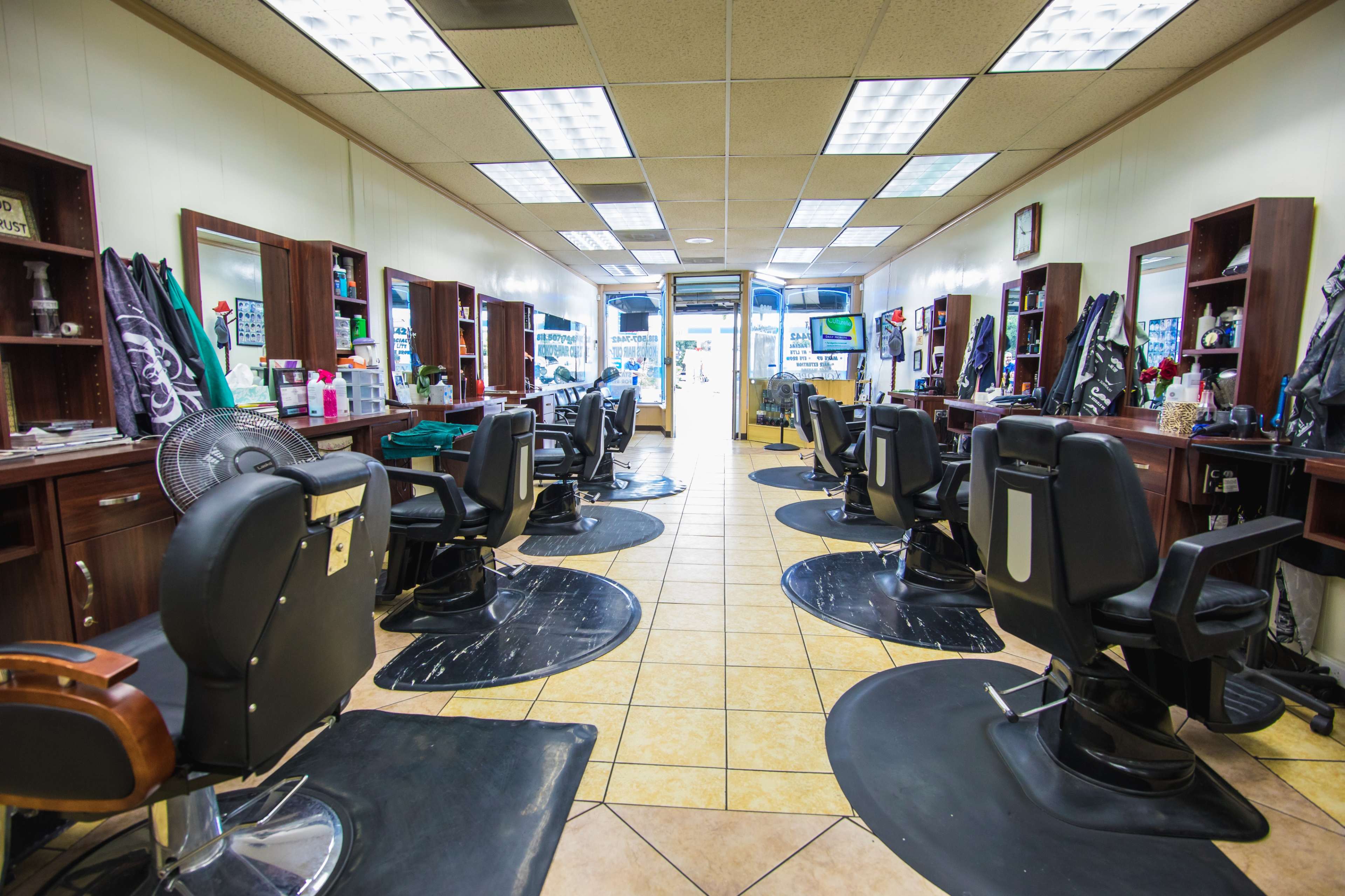 The interior of a barbershop features several styling stations with black chairs, mirrors, and a tiled floor.