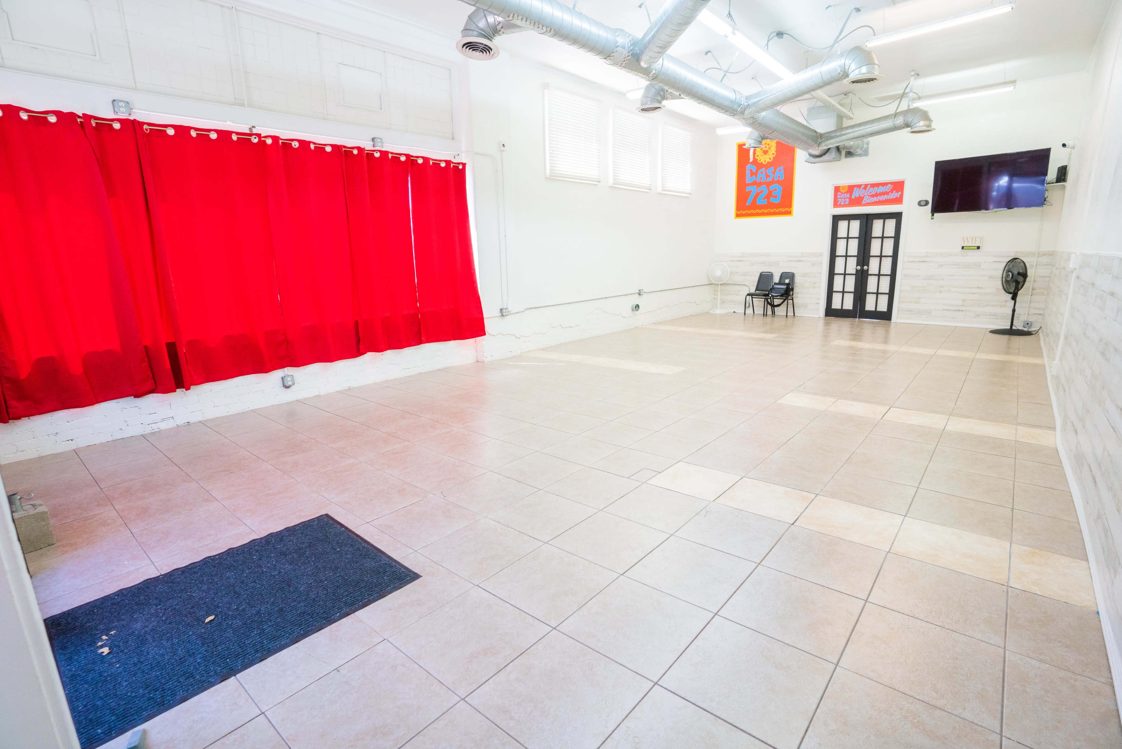 An interior space with tiled flooring, red curtains on one side, and a fan in the corner near a door.