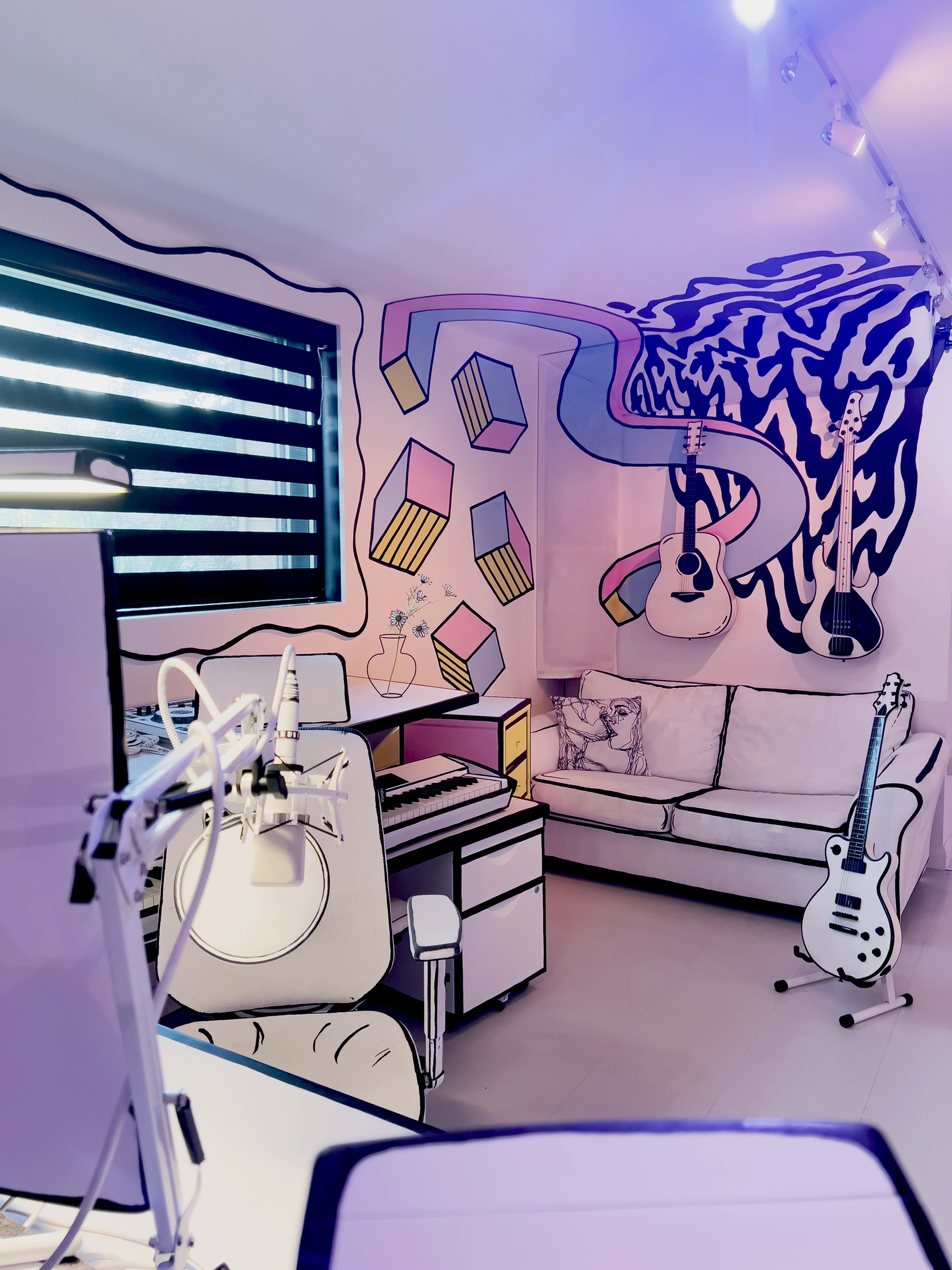 A colorful music studio with a white couch, a keyboard, and guitars displayed on the walls.