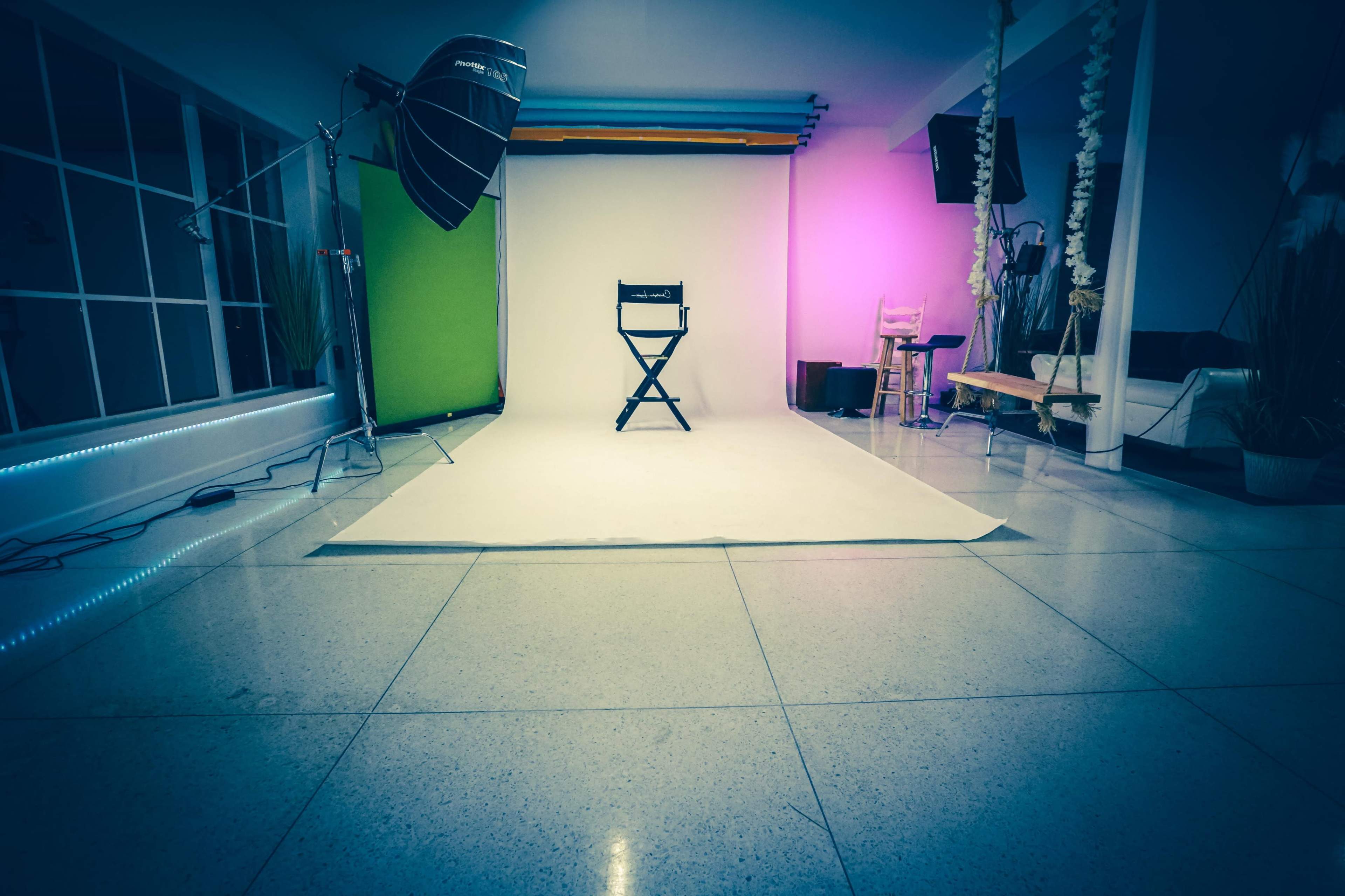 A photography studio with a single director's chair positioned on a light backdrop, surrounded by studio lighting and decor elements.