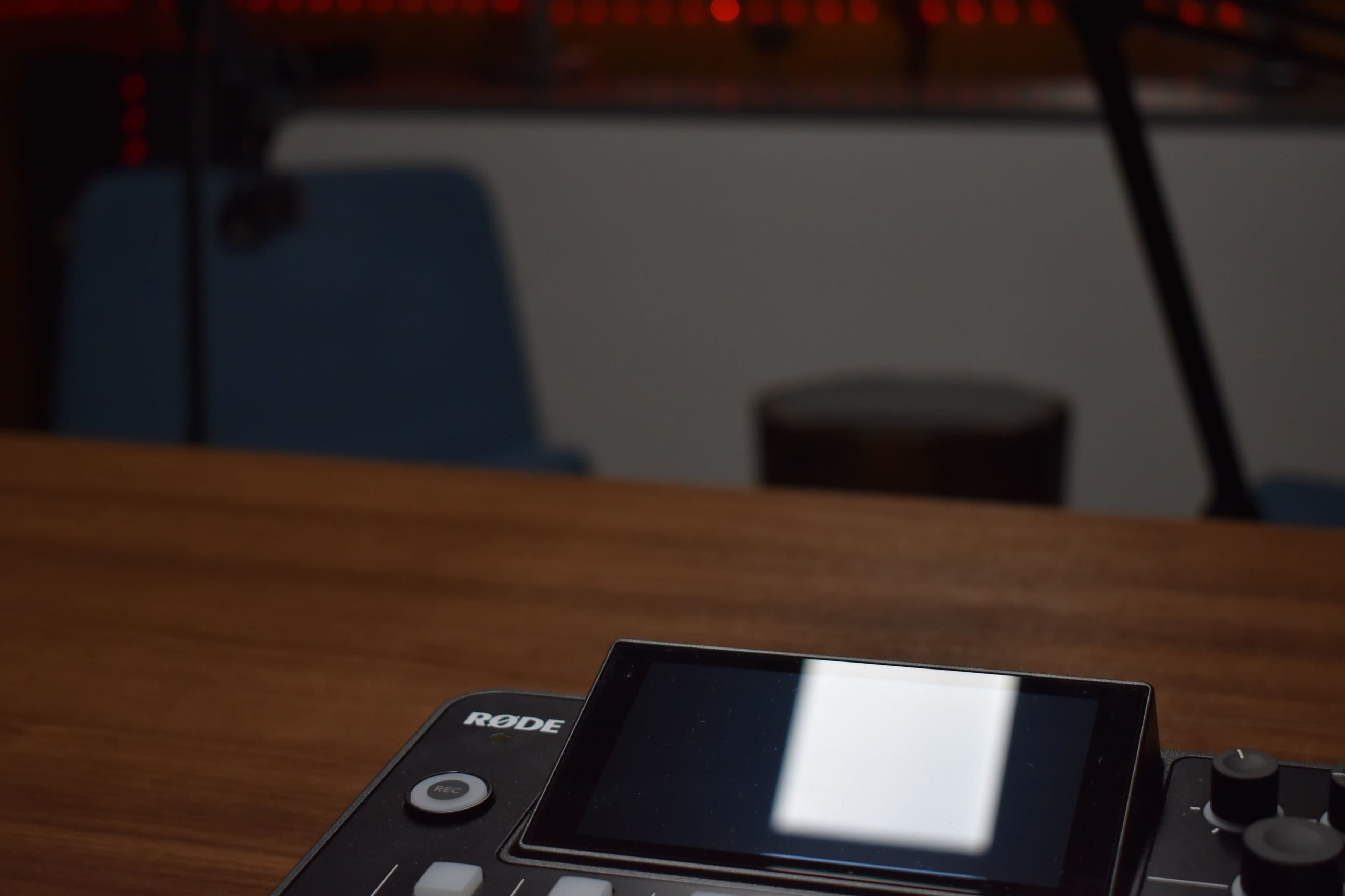 A Rode audio device is positioned on a wooden table with blurred seating and background elements.