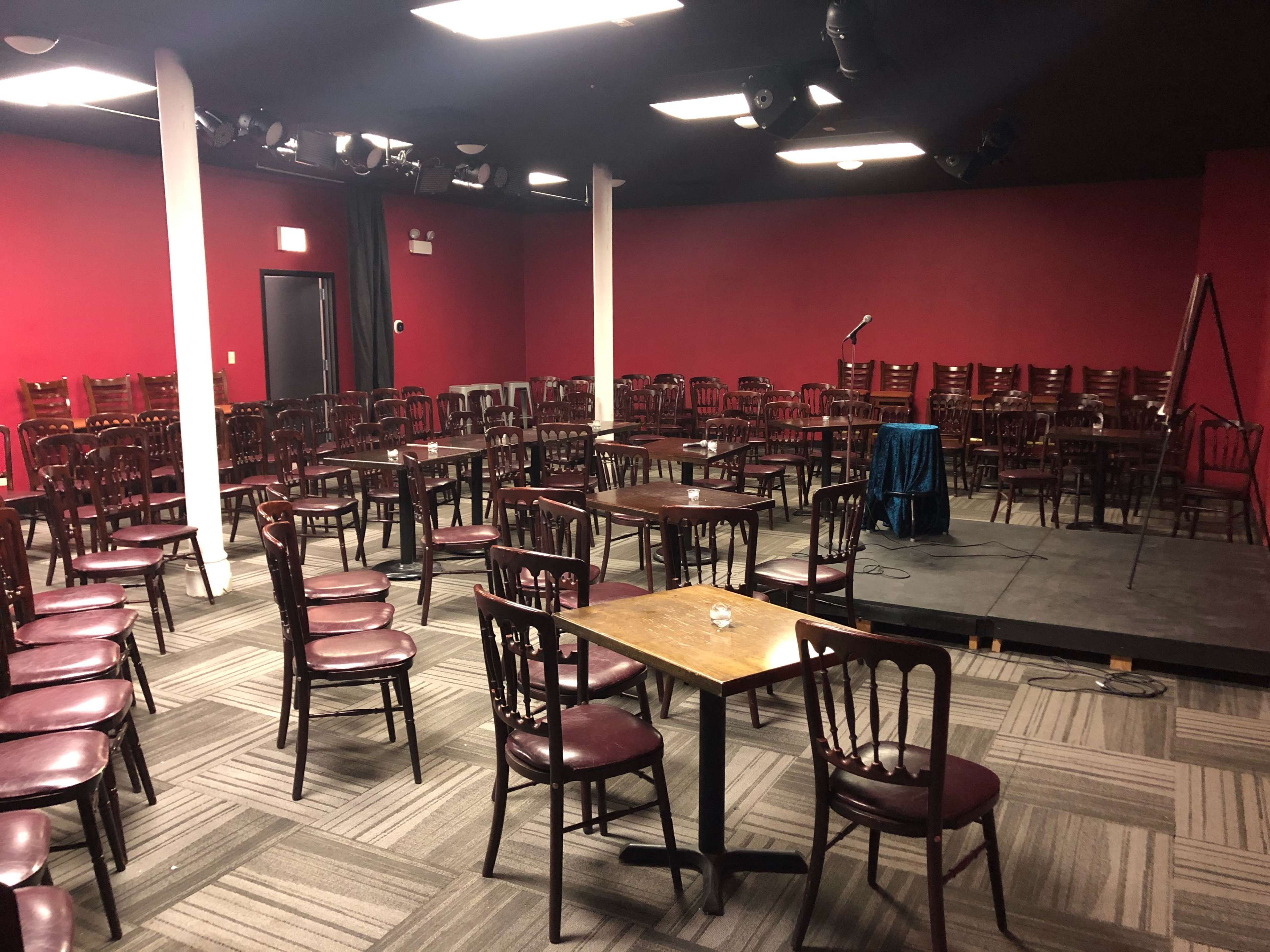 An empty performance space with arranged chairs facing a small stage equipped with a microphone and a table draped in blue.