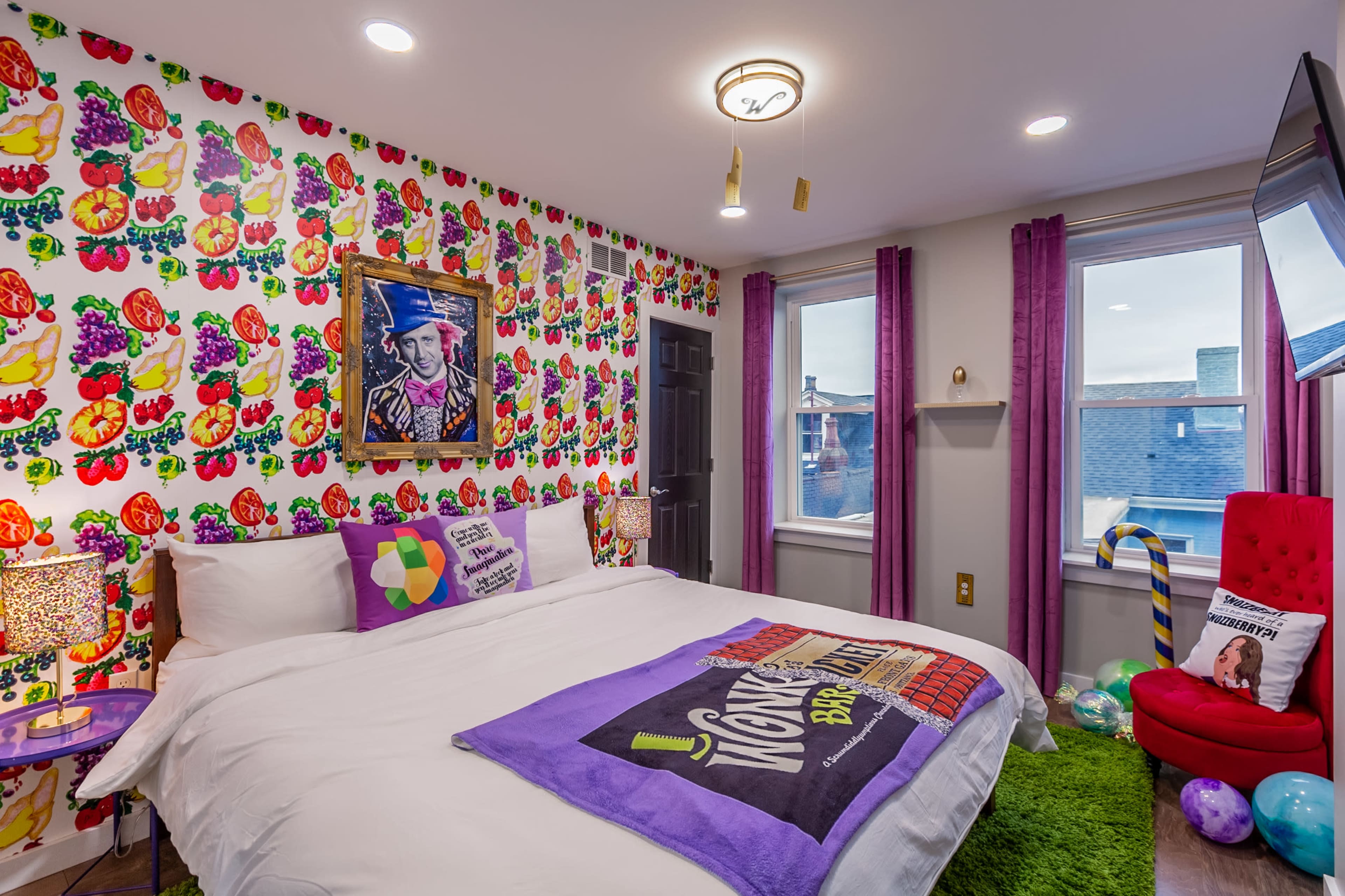 A colorful bedroom features a large bed with a patterned blanket, vibrant flower wallpaper, and various decorative items surrounding it.