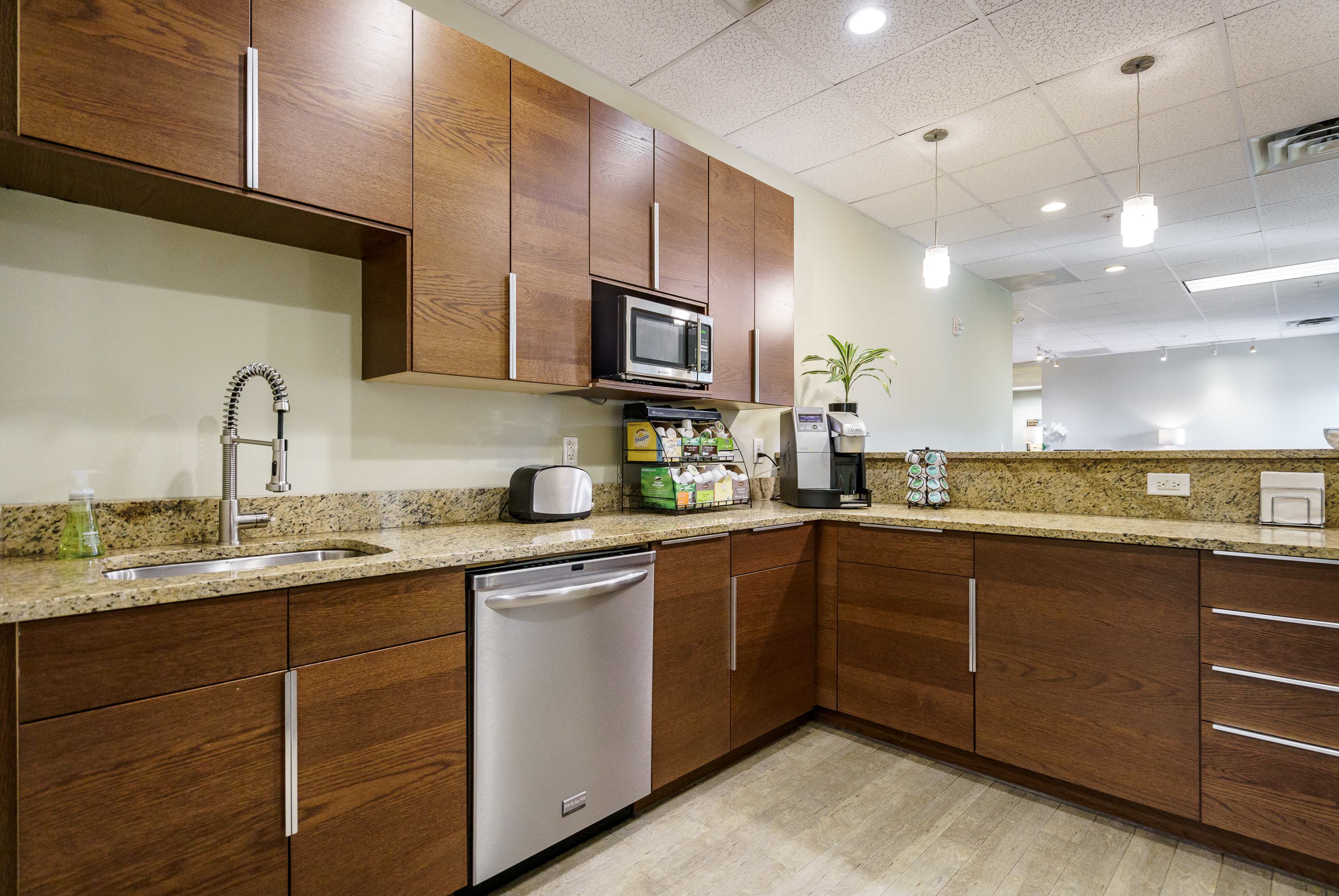 A modern kitchen with wooden cabinets, a stainless steel dishwasher, a microwave, and a countertop adorned with various kitchen appliances and a small plant.