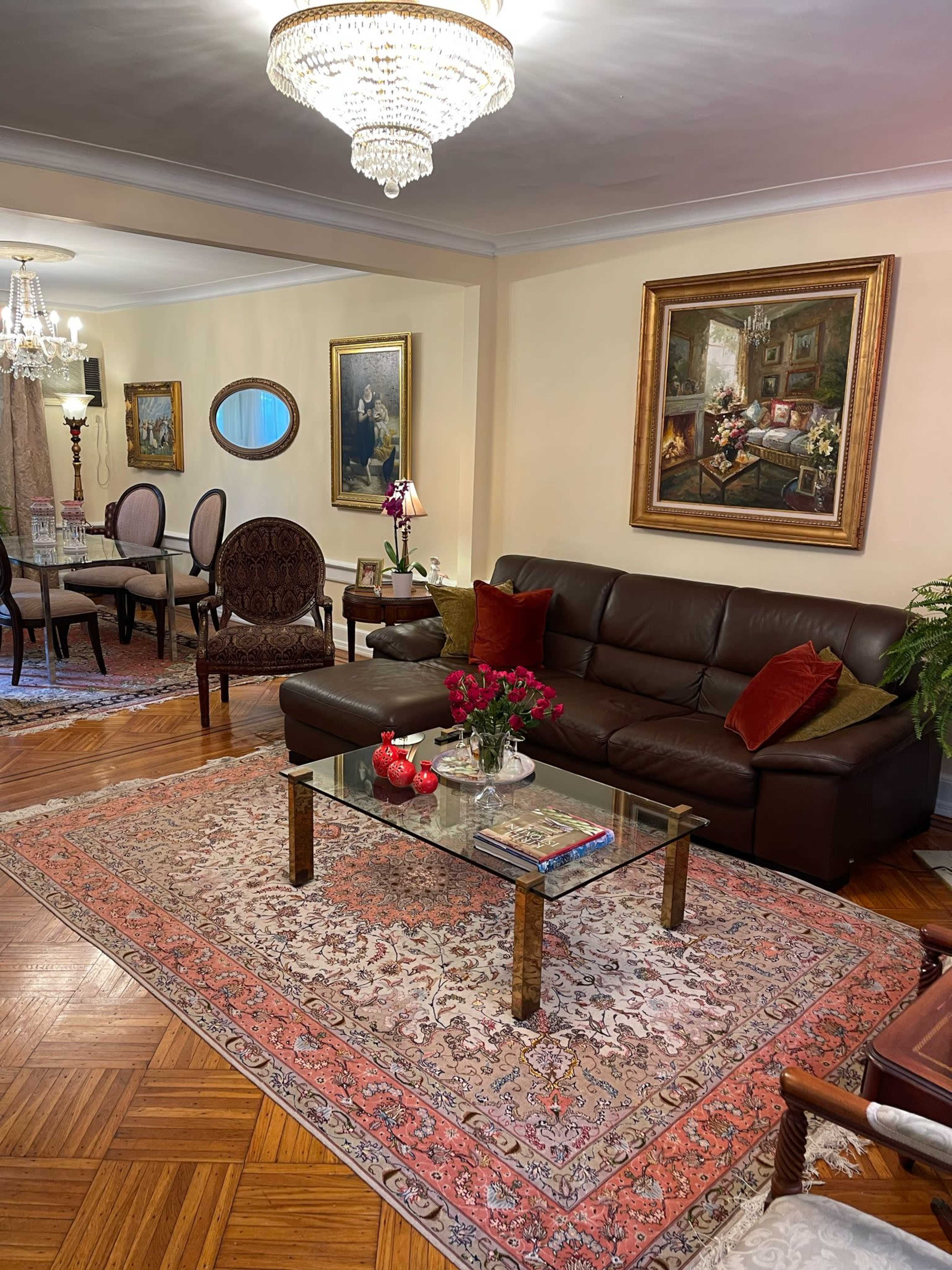 A living room with a dark leather sofa, a glass coffee table adorned with flowers and decorative items, and framed paintings on the walls.