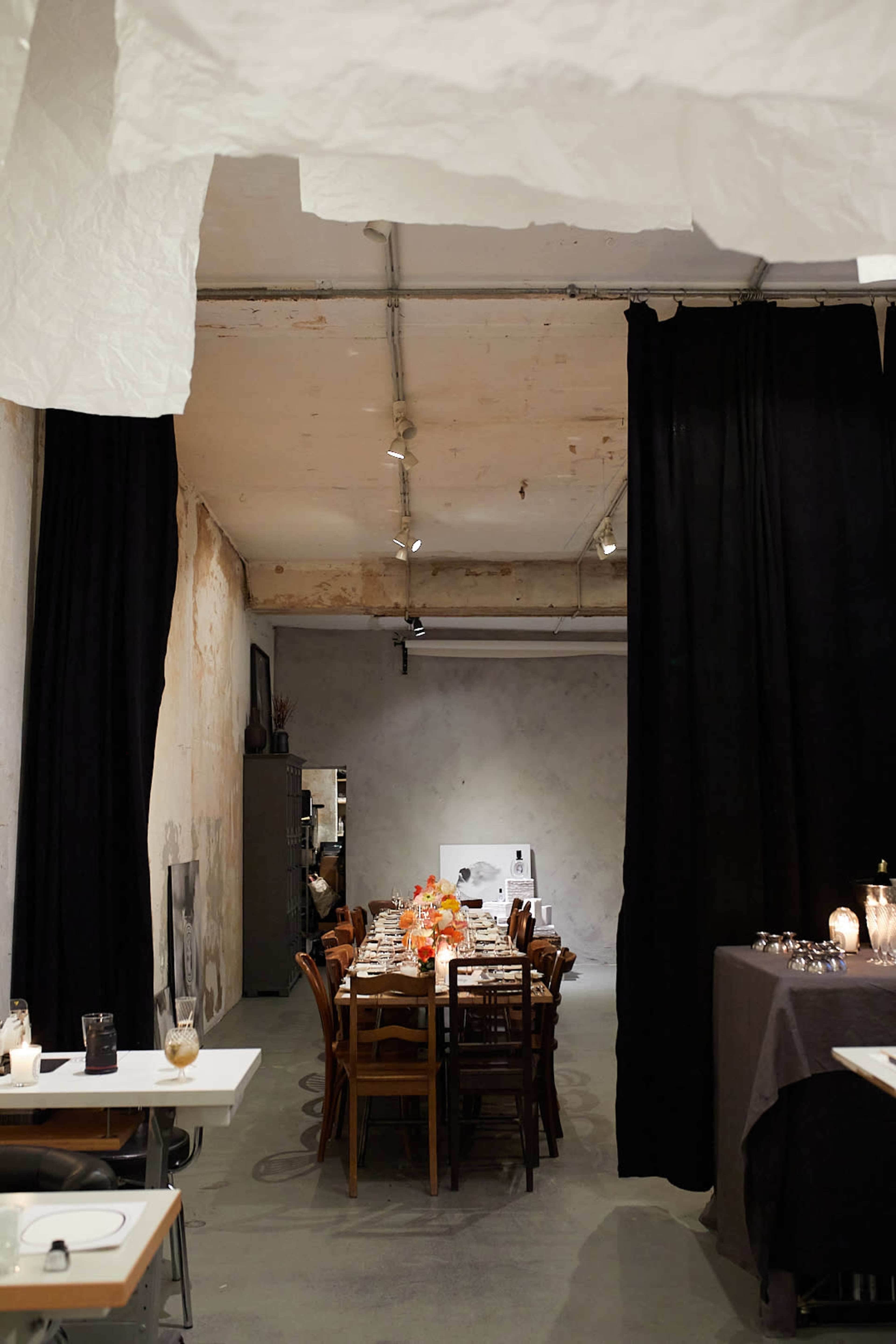 A dining area with a long table set for a meal, surrounded by dark curtains and an unfinished wall.