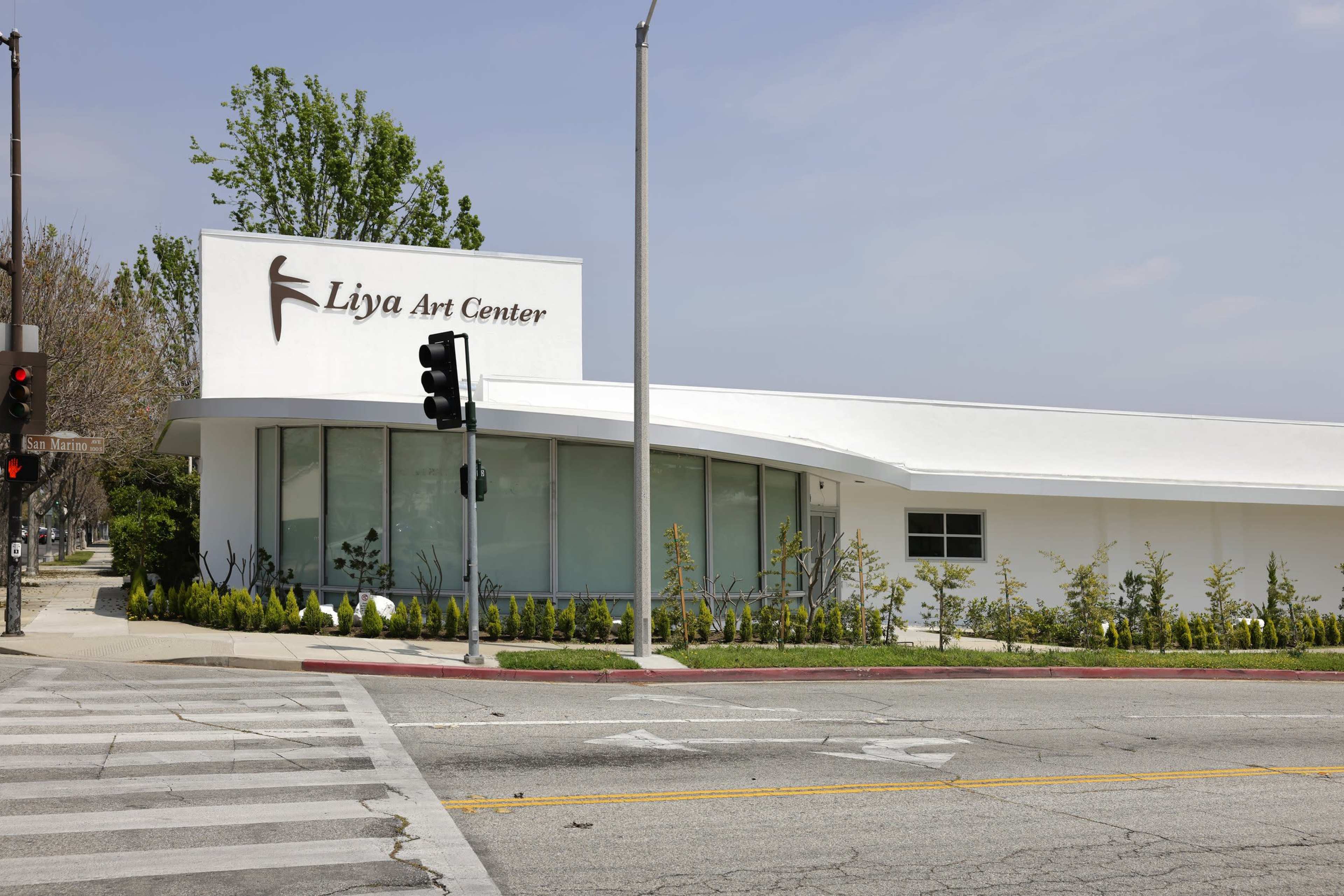 The image shows a modern white building with the signage "Liya Art Center," located at an intersection with traffic lights and greenery in the foreground.
