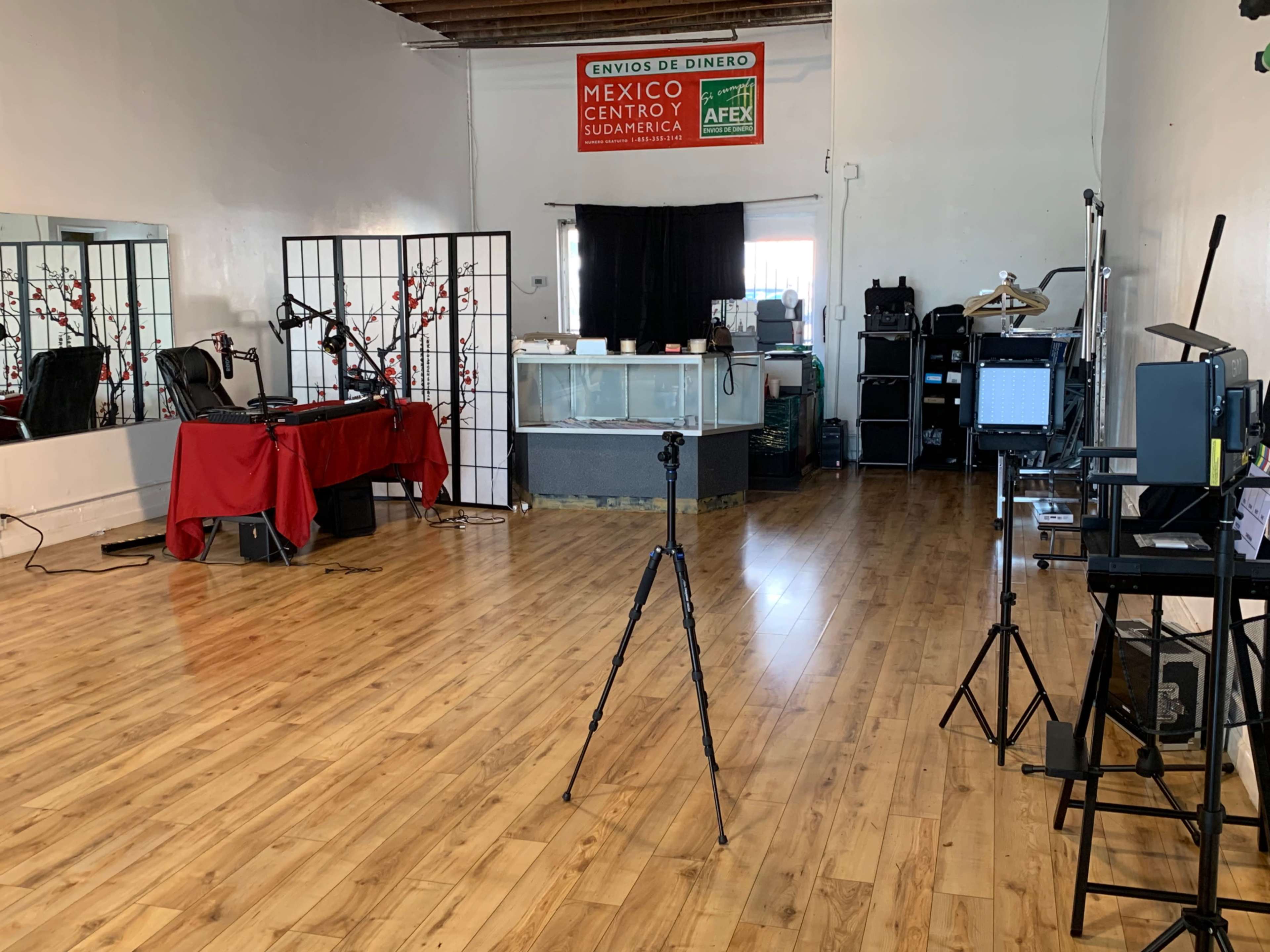 A spacious room with wooden flooring, featuring a reception area, a red tablecloth, and various equipment set up for photography or video recording.