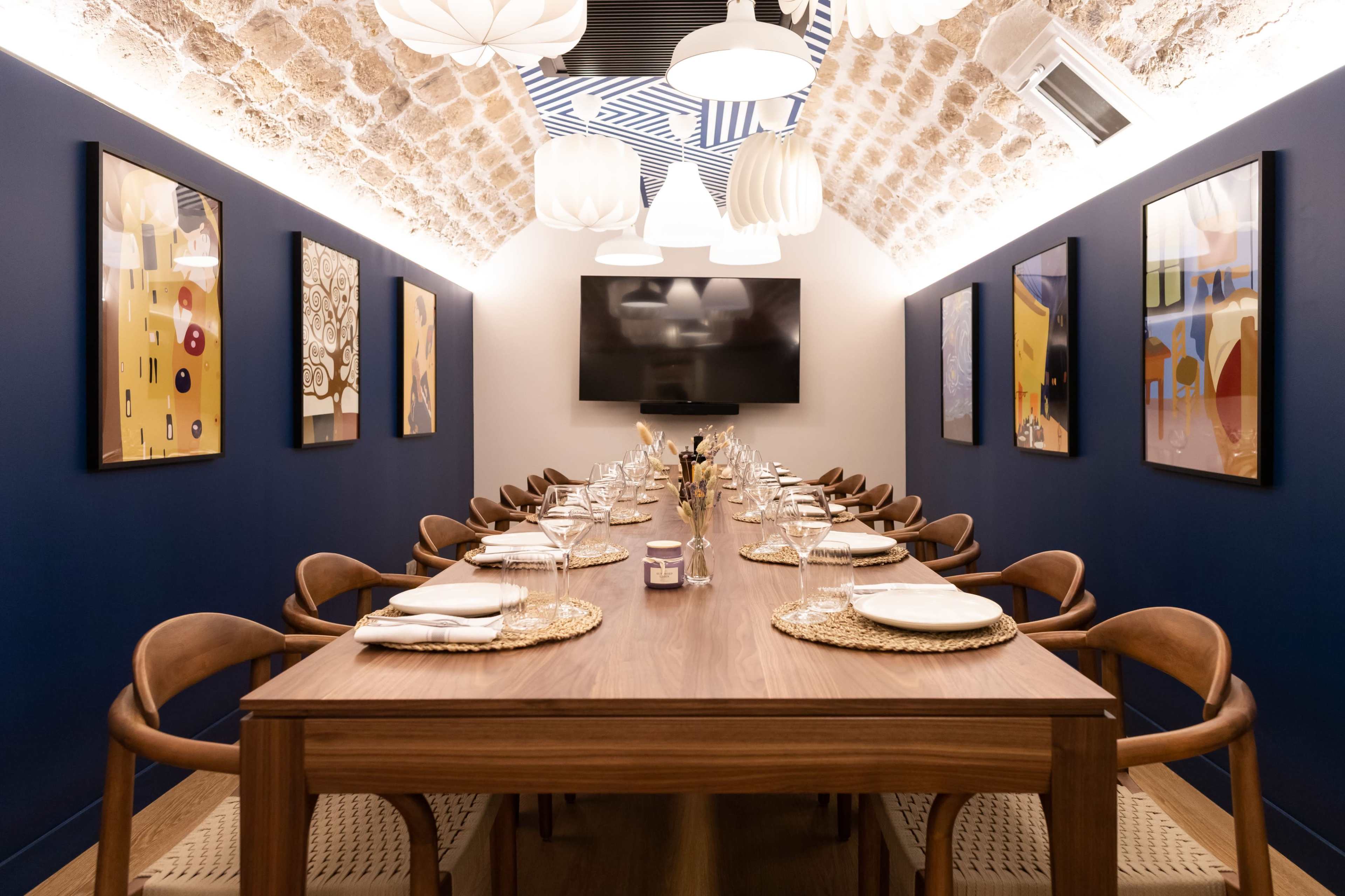 A modern dining room with a long wooden table set for a meal, surrounded by wooden chairs, under a vaulted ceiling with decorative wall art and pendant lights.