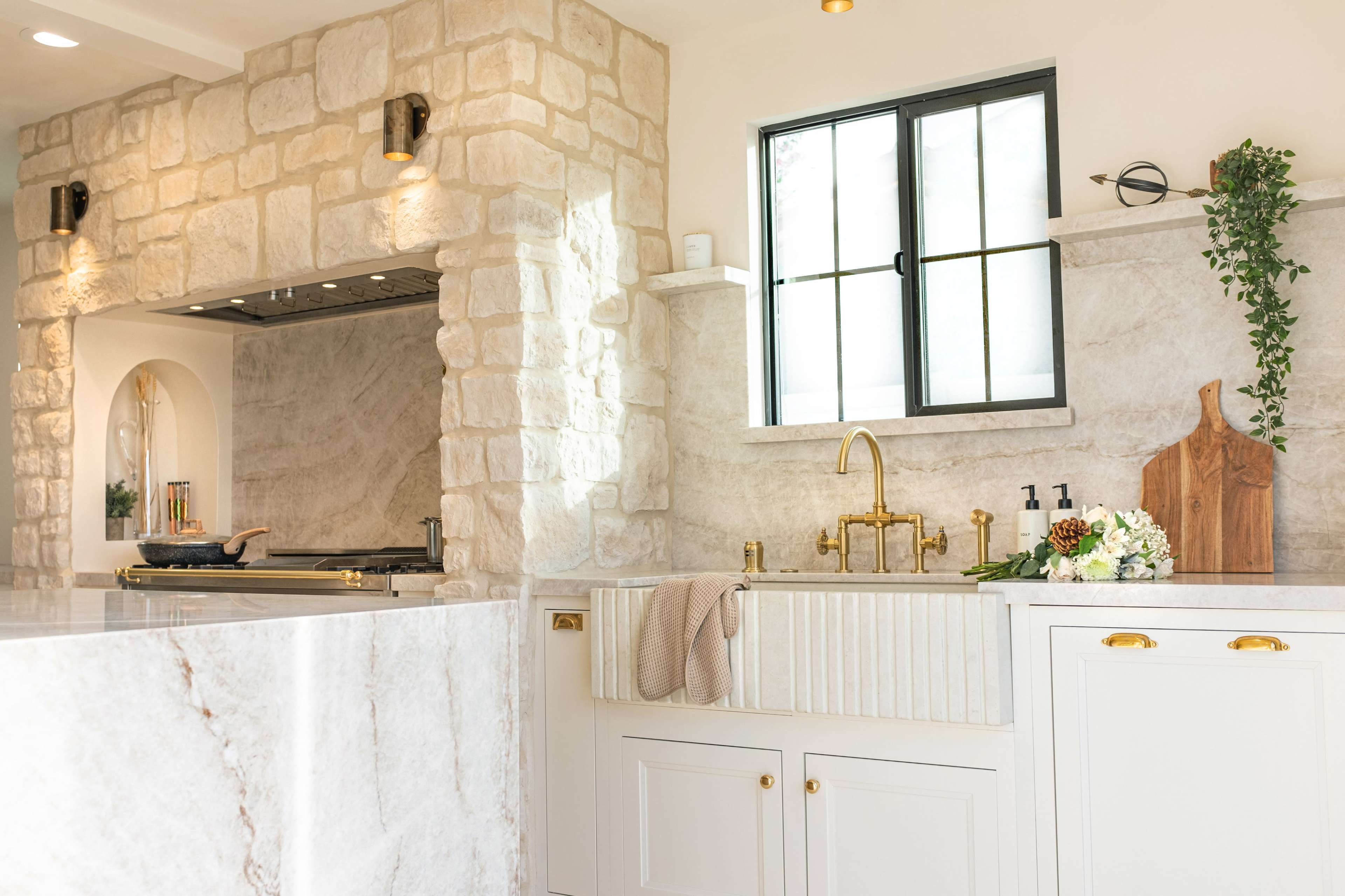 A kitchen with a marble countertop, a farmhouse sink, stone walls, and modern fixtures.