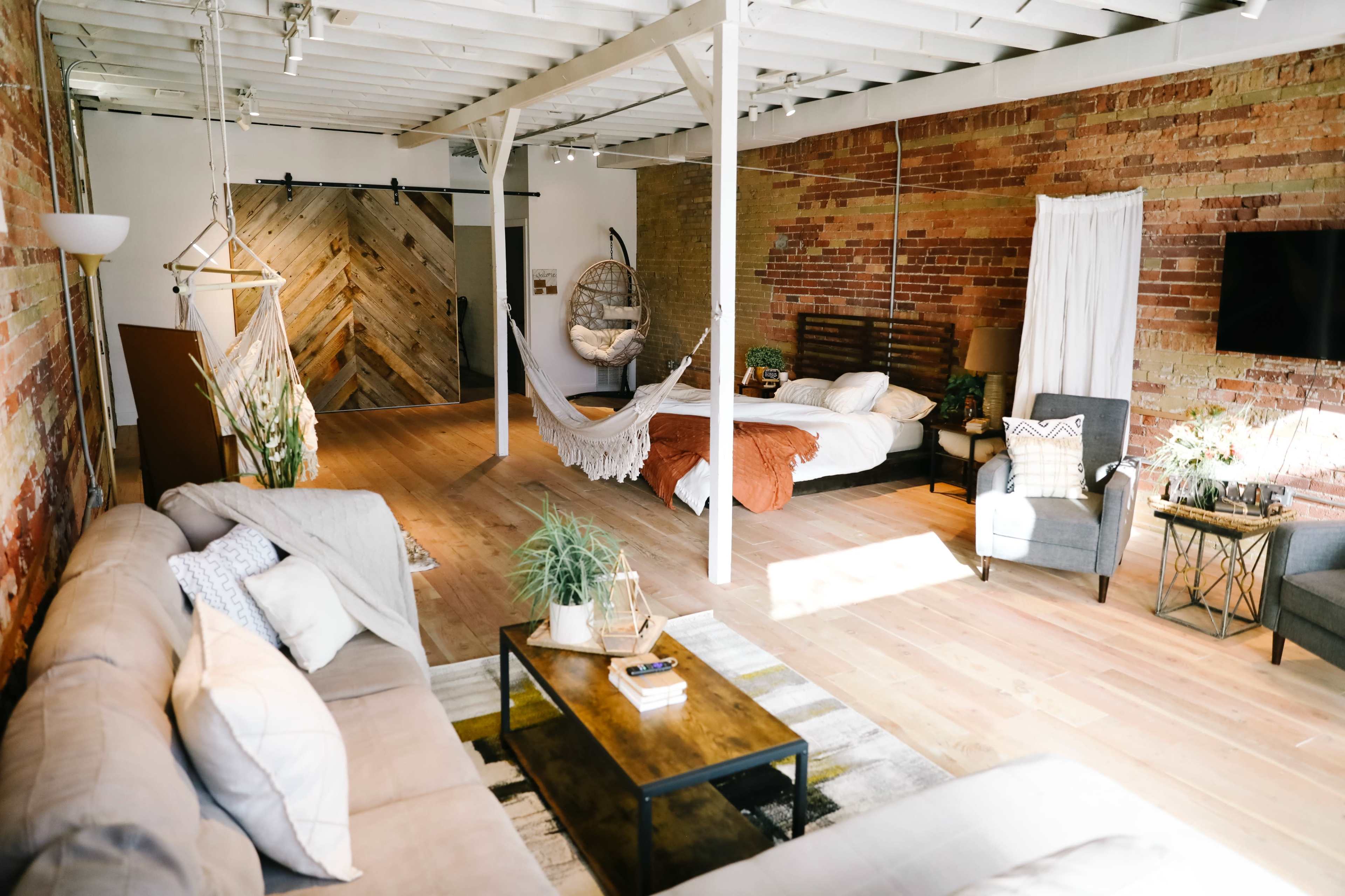 A spacious room featuring a mix of rustic brick and wooden walls, with a large bed, a sofa, and a hanging chair.