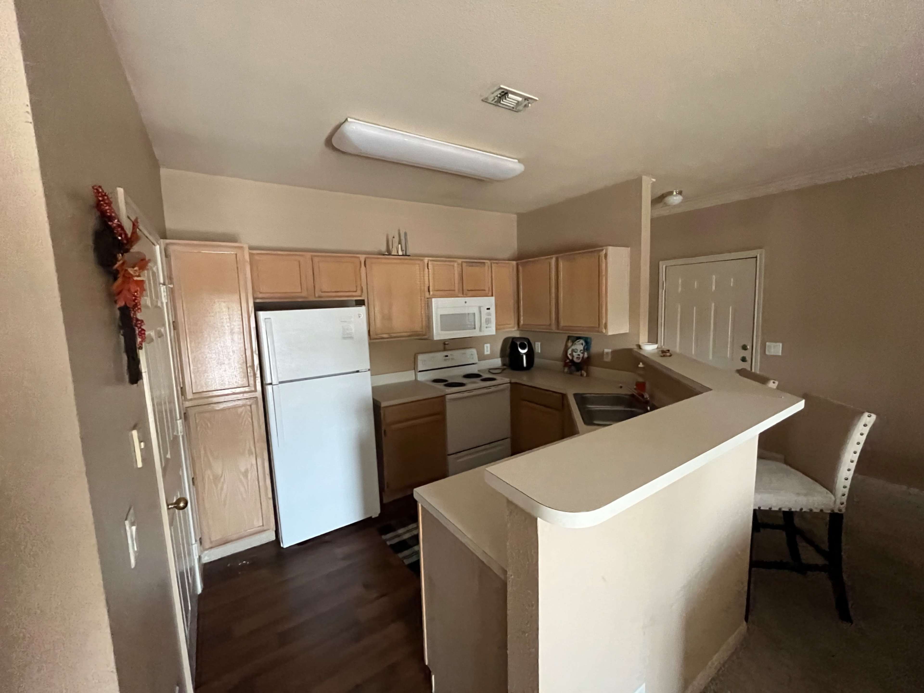A kitchen features light wooden cabinets, white appliances, and a small breakfast bar with a chair.