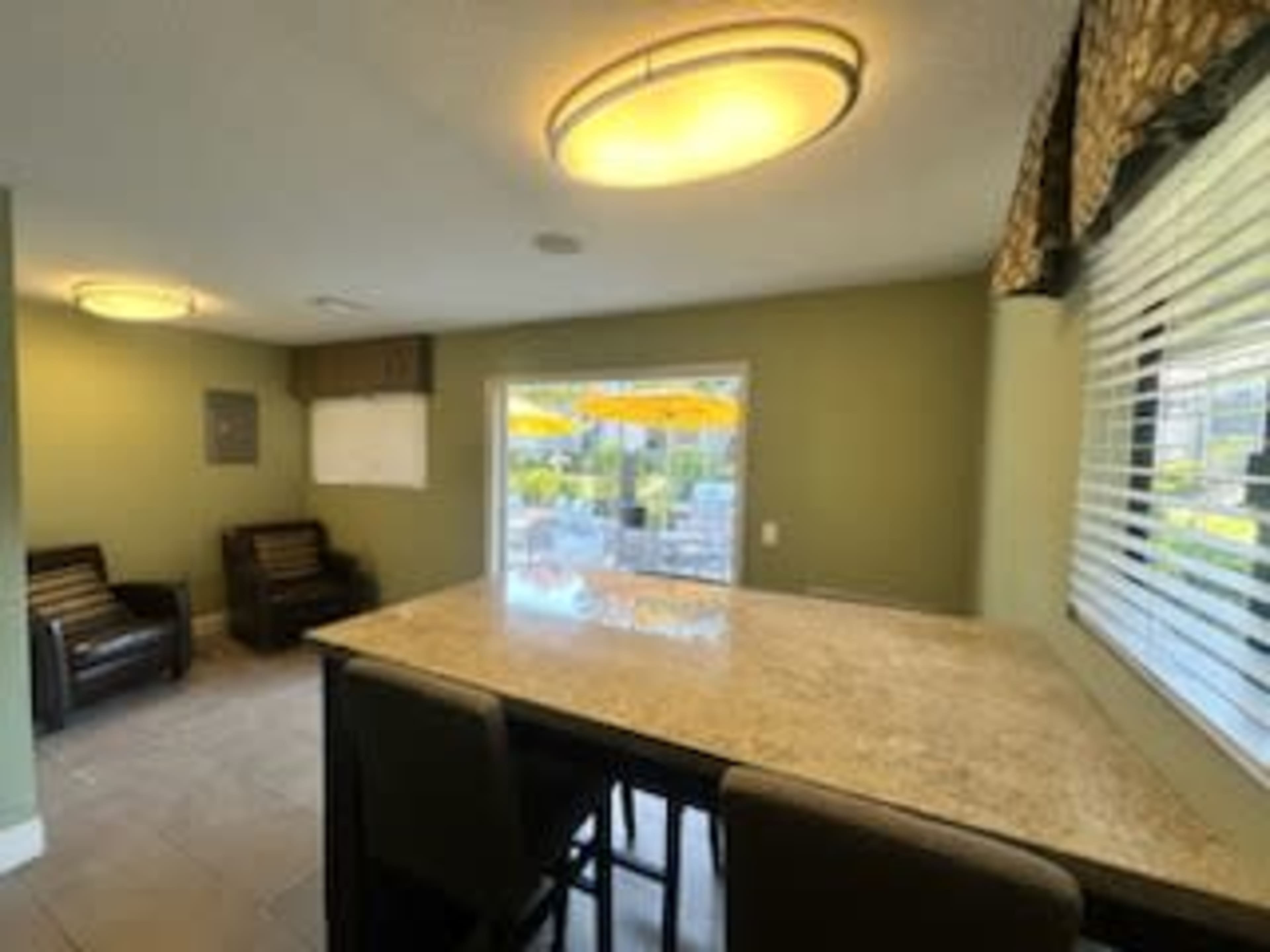 A well-lit room with a granite countertop bar and seating, adjacent to a window overlooking an outdoor area with umbrellas.