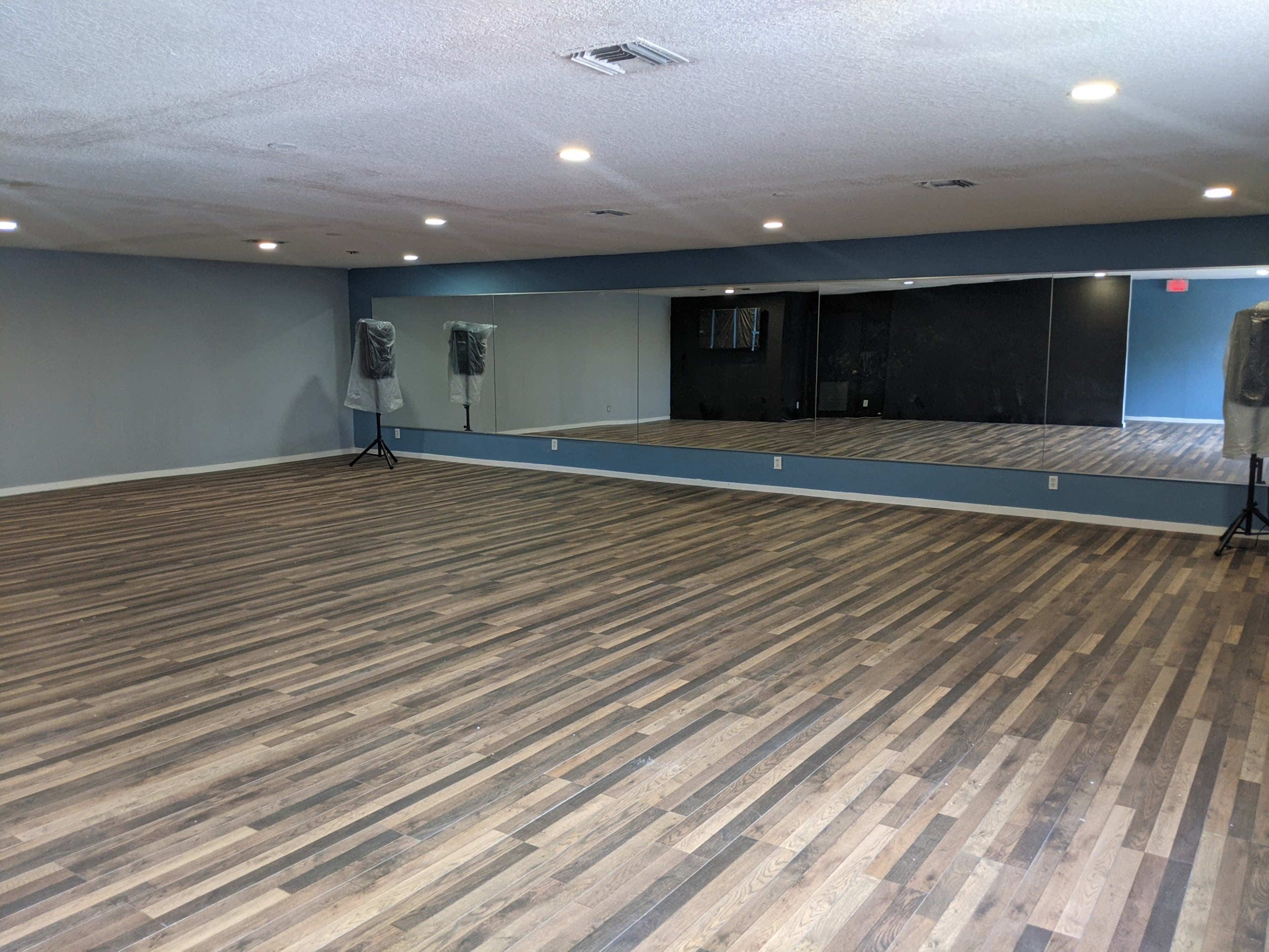 An empty dance studio with wooden flooring and large mirrors on one wall.