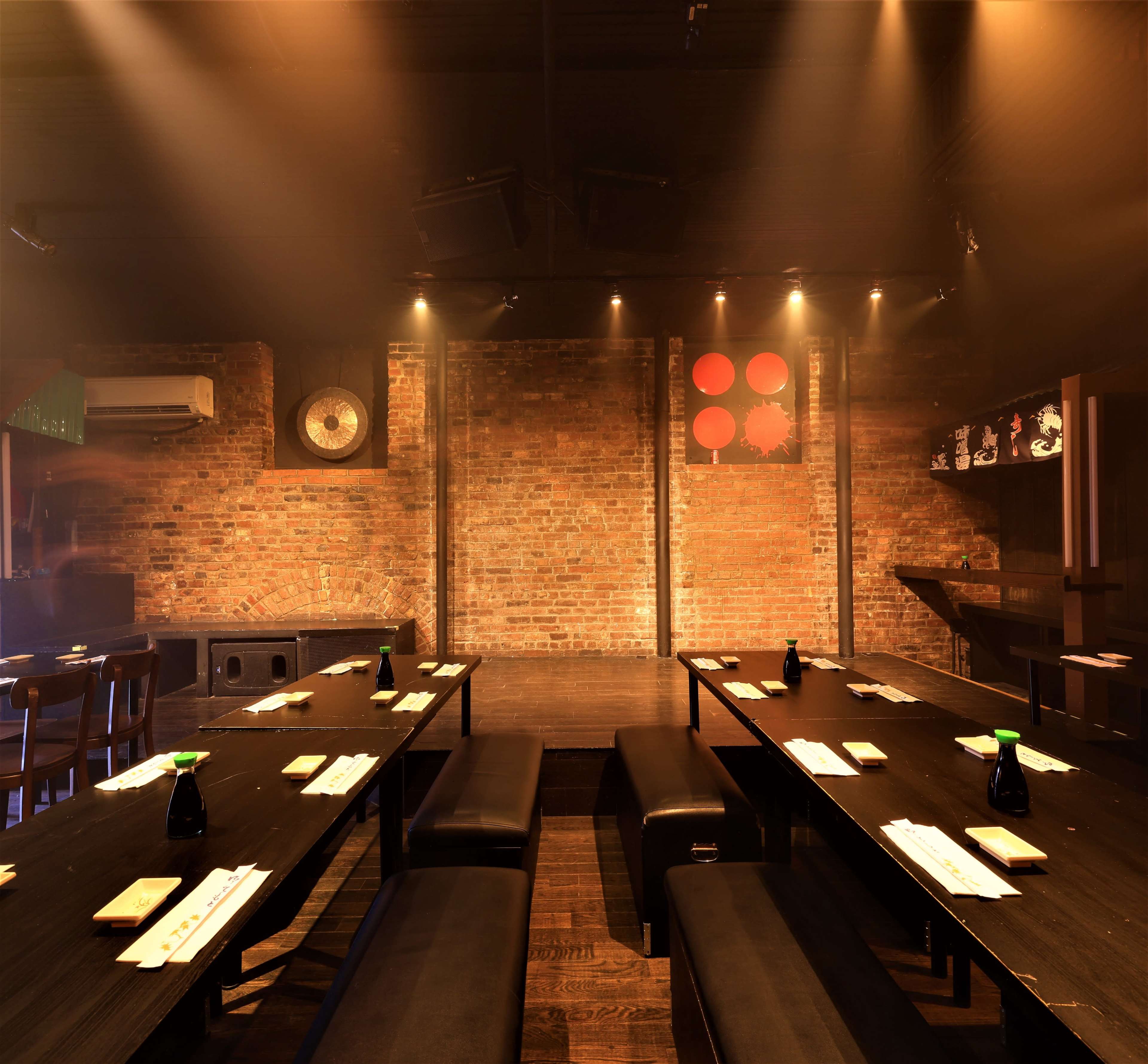 A dimly lit restaurant with wooden benches arranged along tables, exposed brick walls, and red circular art pieces.