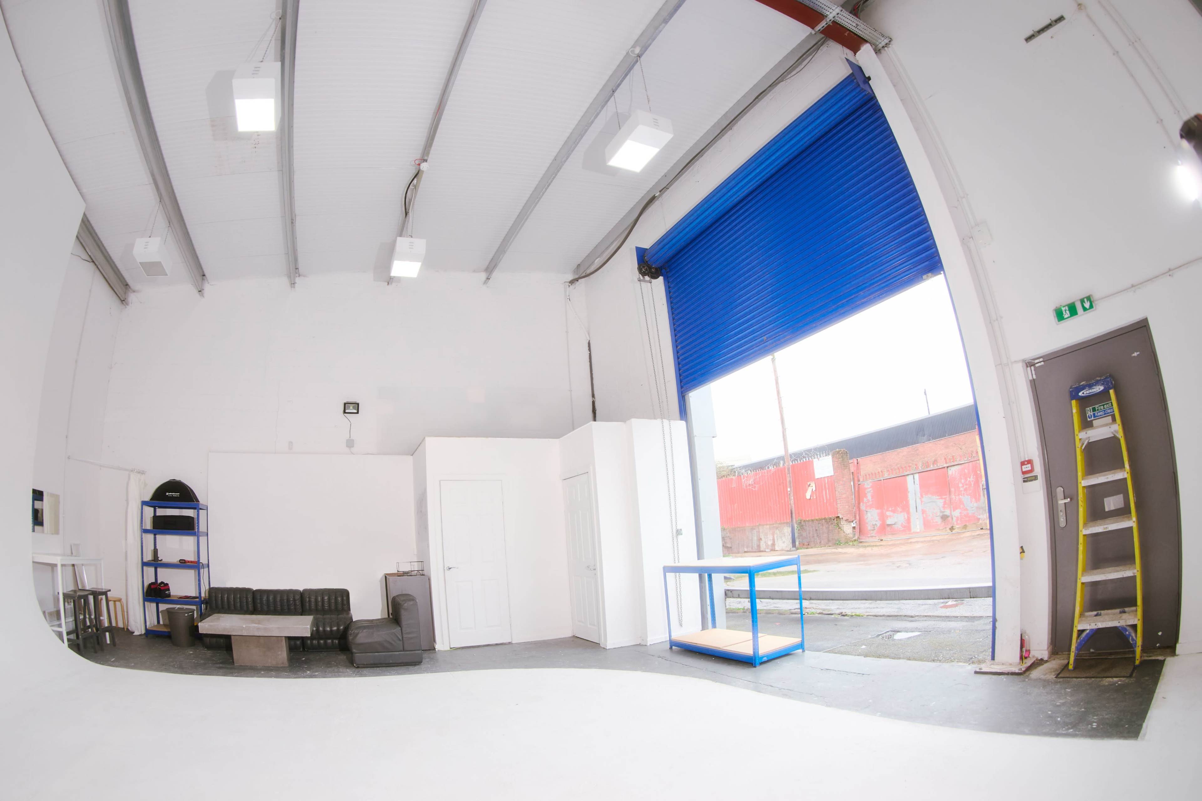 A spacious white interior with a black couch, a white door, a blue rolling door, and a wooden table against one wall, along with a ladder positioned nearby.