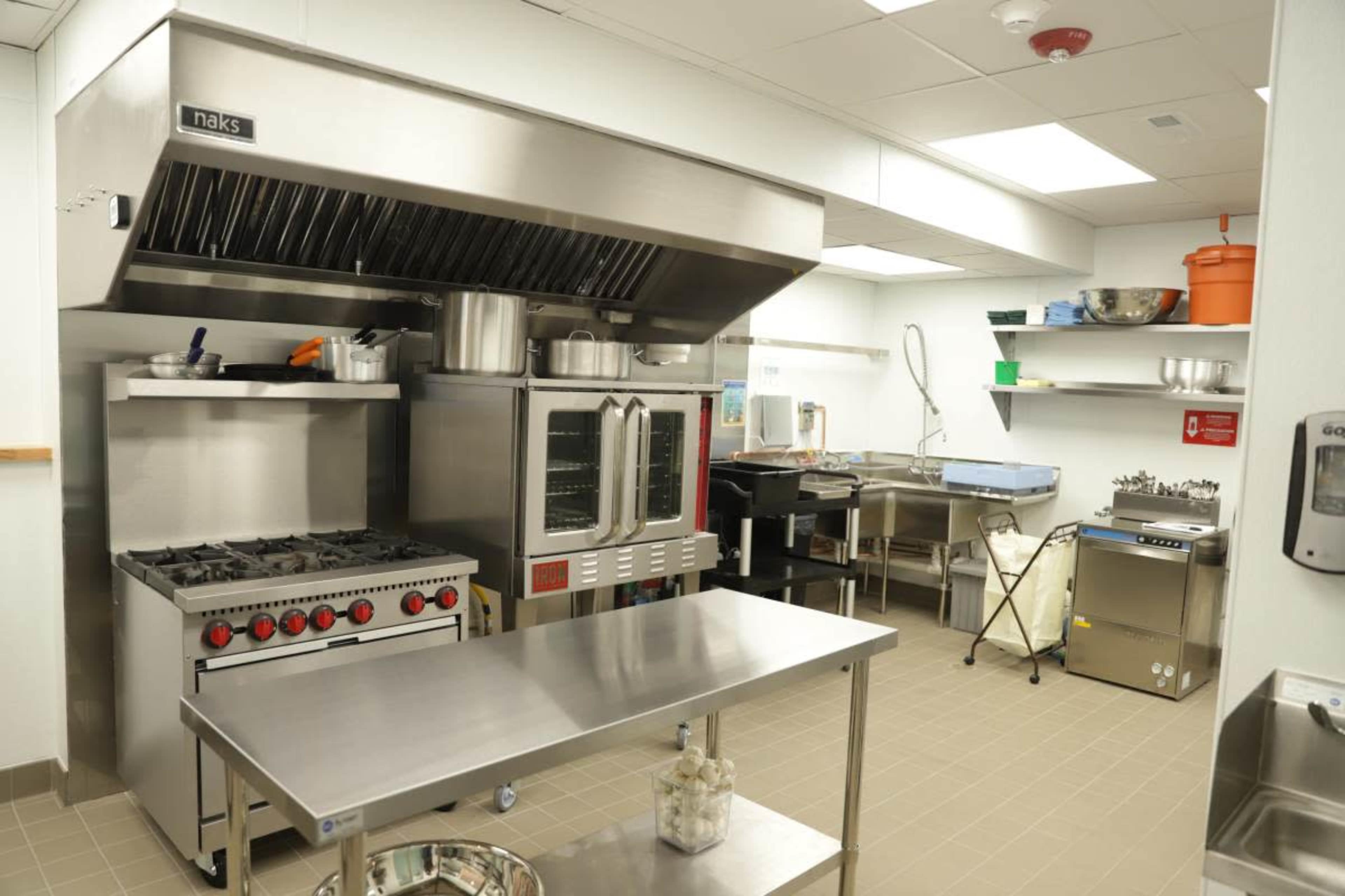 The image shows a commercial kitchen equipped with stainless steel appliances, including a gas stove, oven, and multiple work surfaces.