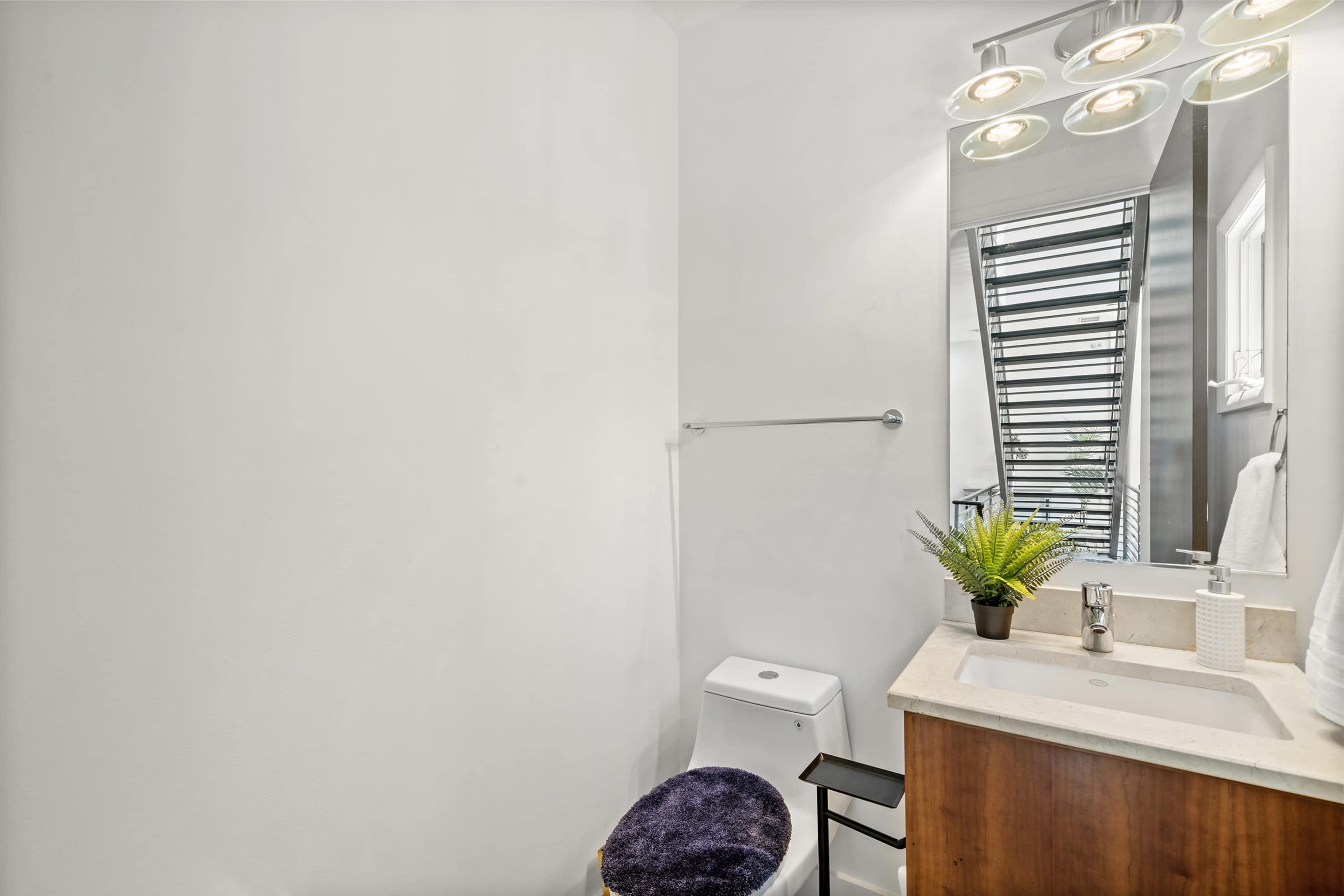 A modern bathroom features a toilet, a sink with a countertop, and a mirror, along with a small potted plant on the sink.