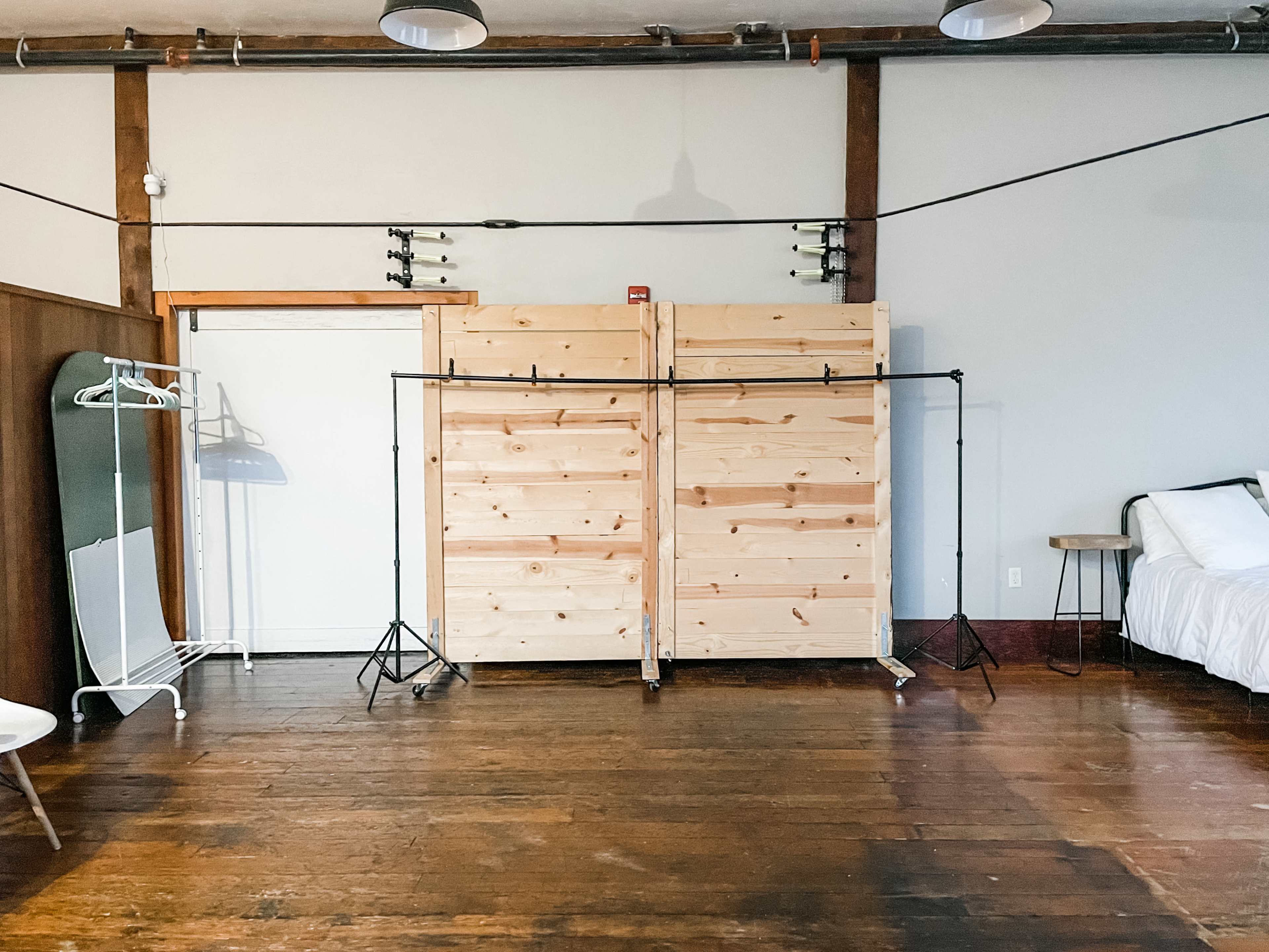 A spacious room with wooden flooring featuring a set of double wooden doors, a clothing rack, and a bed against the wall.
