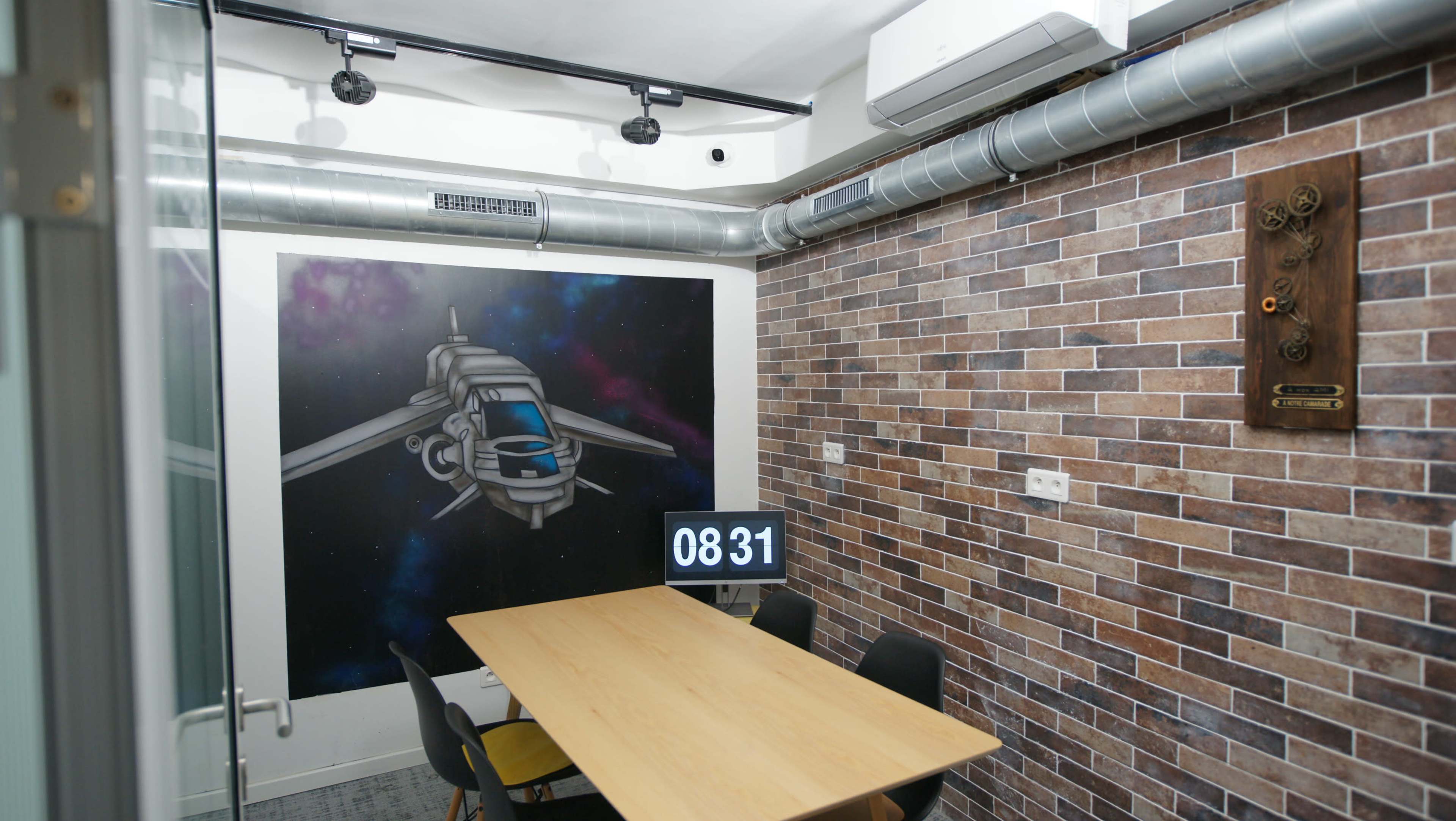 A modern meeting room with a brick wall, a large wooden table, and a mural of a spaceship.