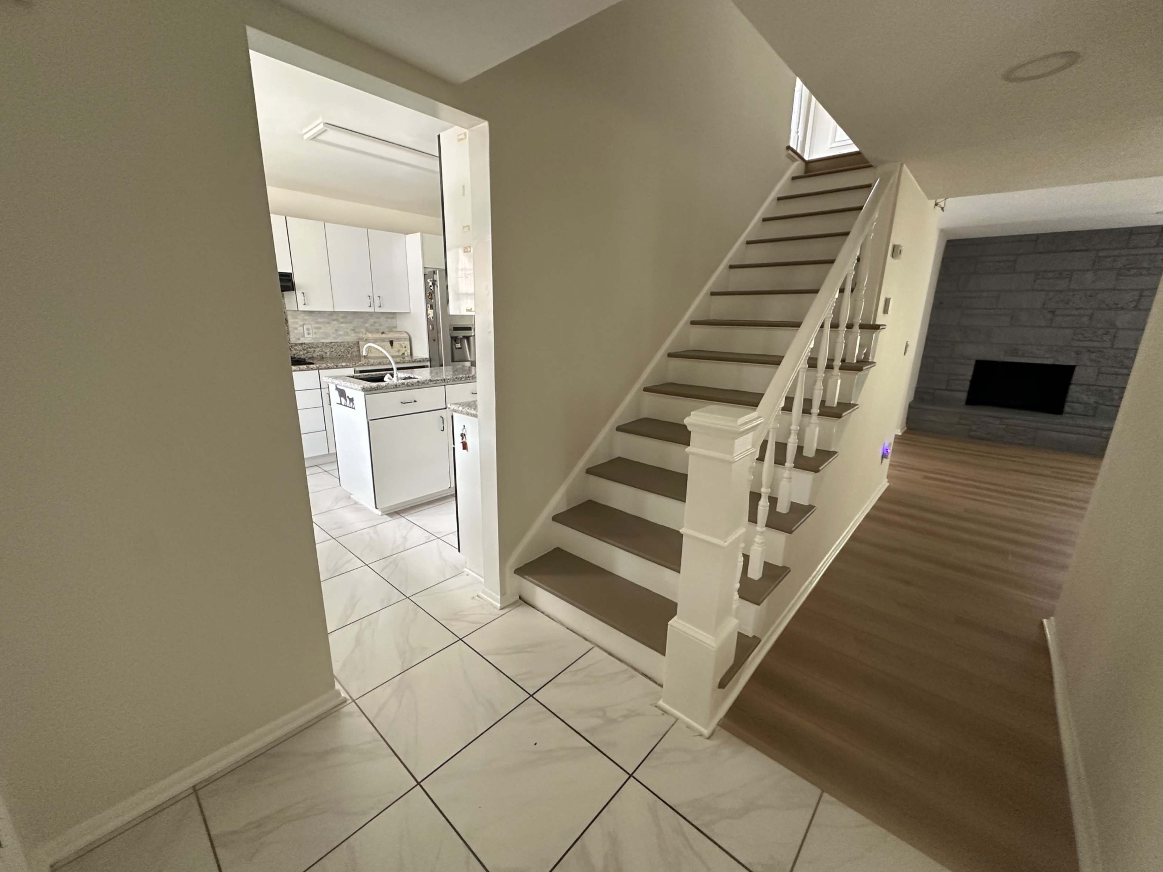 The image shows a bright hallway with a staircase leading to an upper level, adjacent to a kitchen area visible through an open doorway.